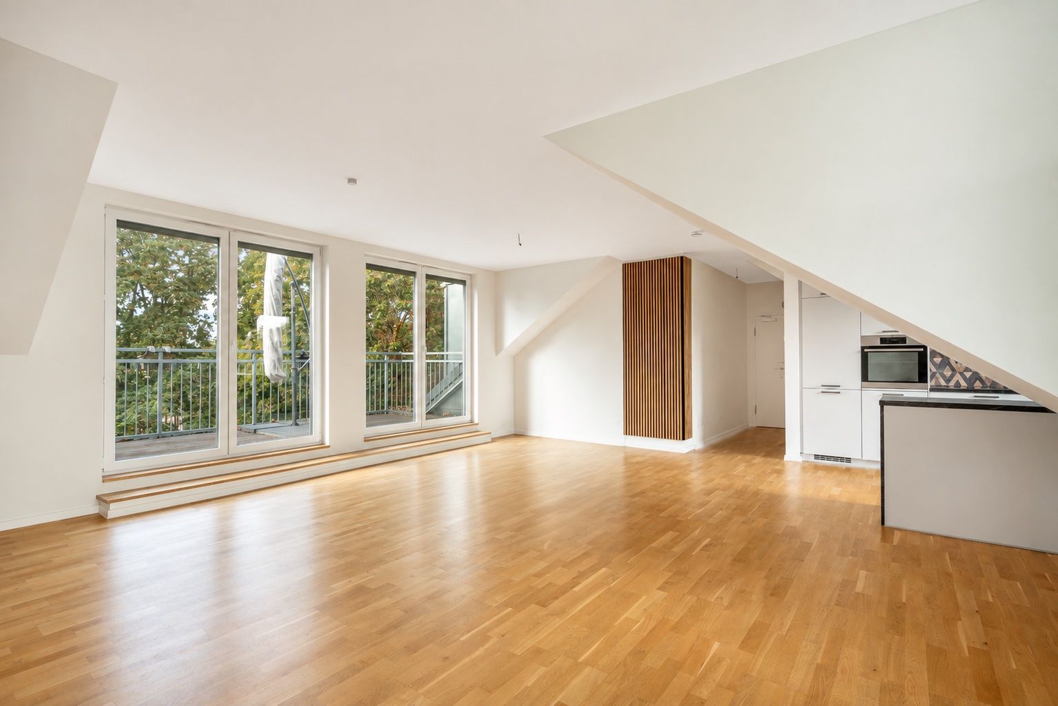 Helles Wohnzimmer mit Parkettboden, großen Fenstern und integrierter offener Küche.