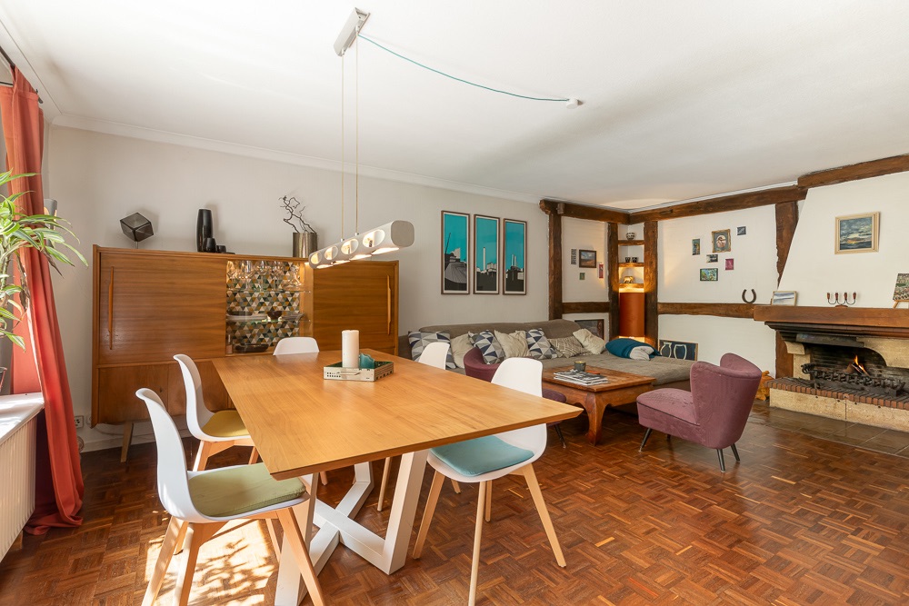 Helles Wohnzimmer mit Esstisch, Stühlen, Sofa, Kamin und Parkettboden.