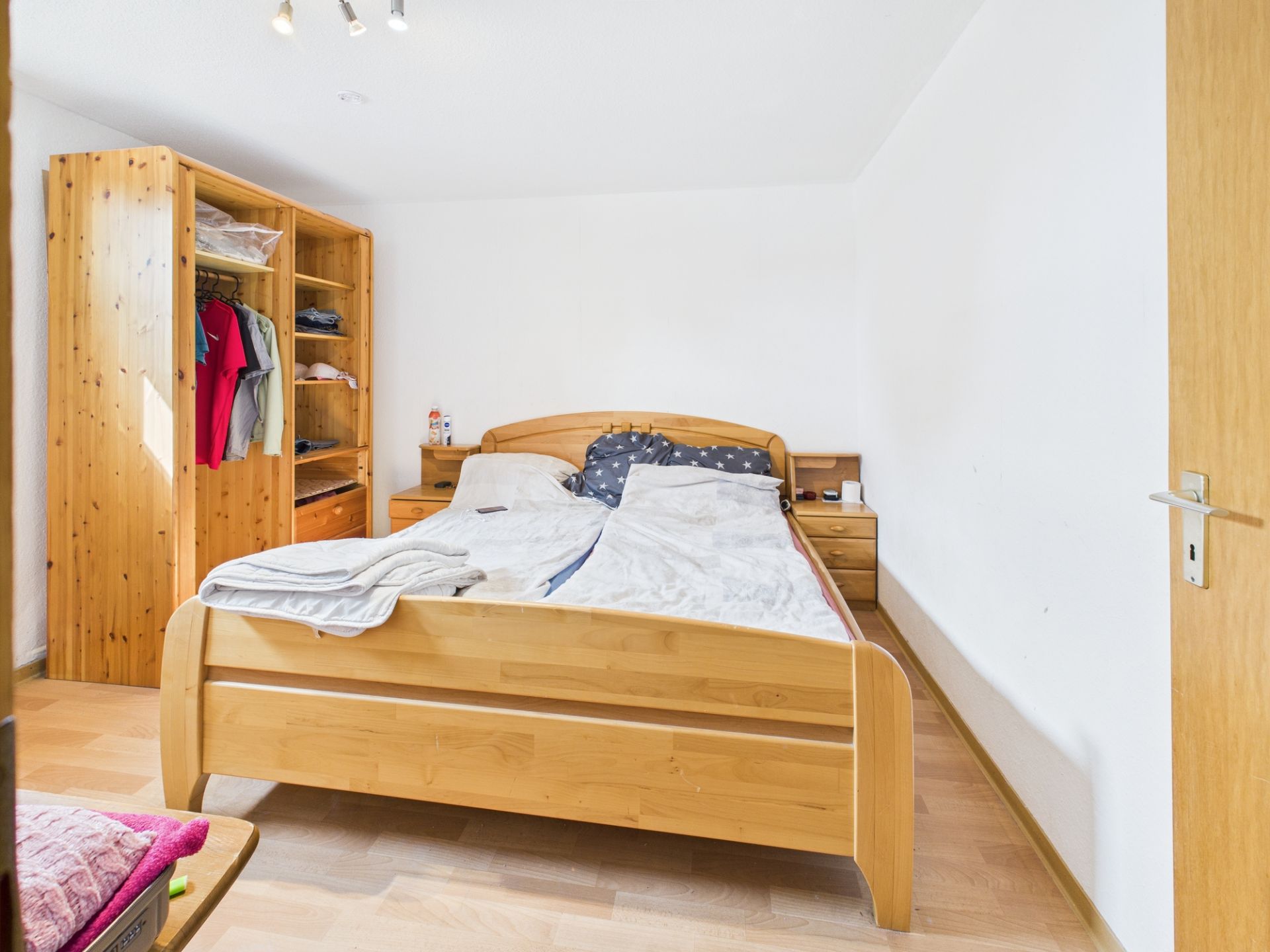 Schlafzimmer mit Holzbett, offenem Kleiderschrank und Nachttischen.