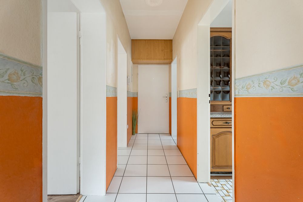 Heller Flur mit orange-weißen Wänden, weißen Fliesen und mehreren Türen.