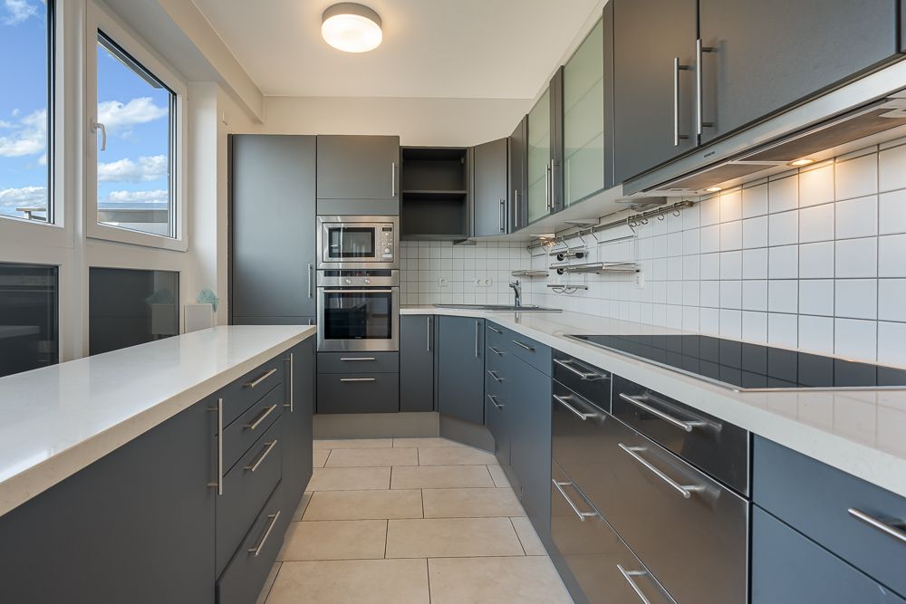 Moderne Einbauküche mit grauen Schränken, weißen Arbeitsplatten und großem Fenster.
