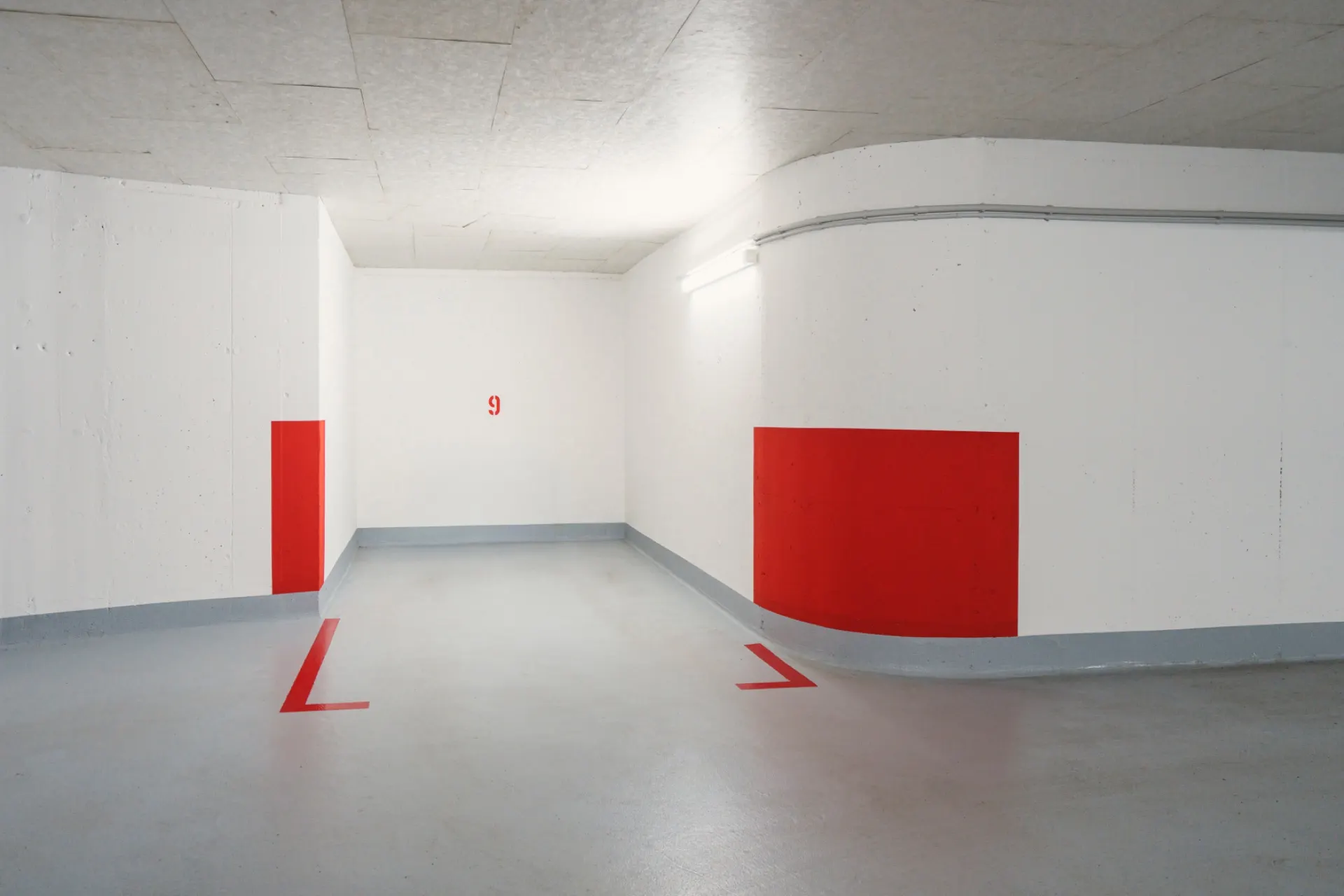 Leerer, heller Parkplatz in einer Tiefgarage mit roten Markierungen und der Nummer 9 an der Wand.