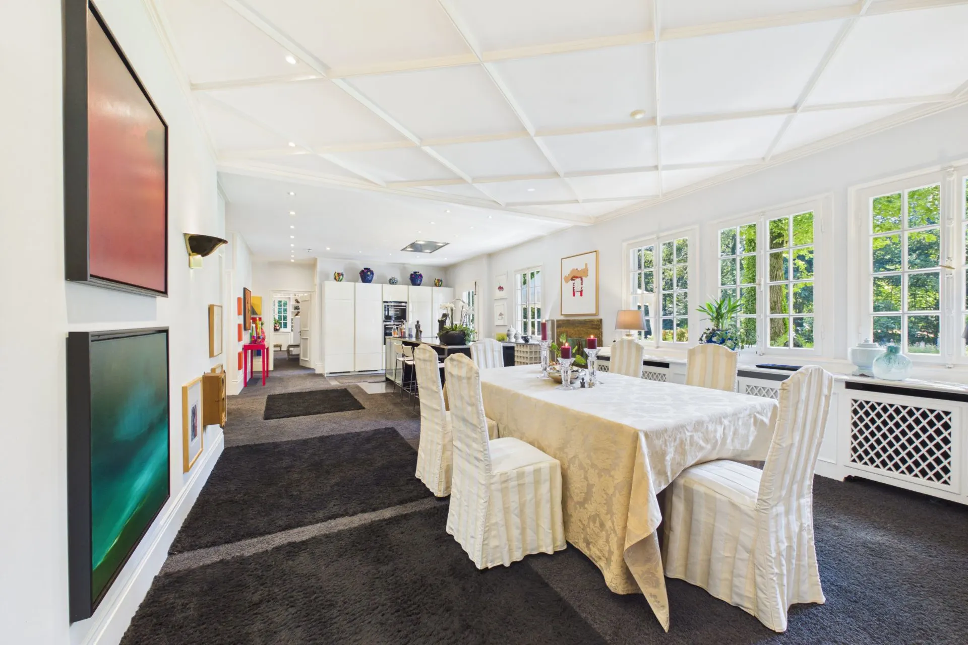 Großes Esszimmer mit langem Tisch, sechs Stühlen und großen Fenstern, viel Tageslicht.