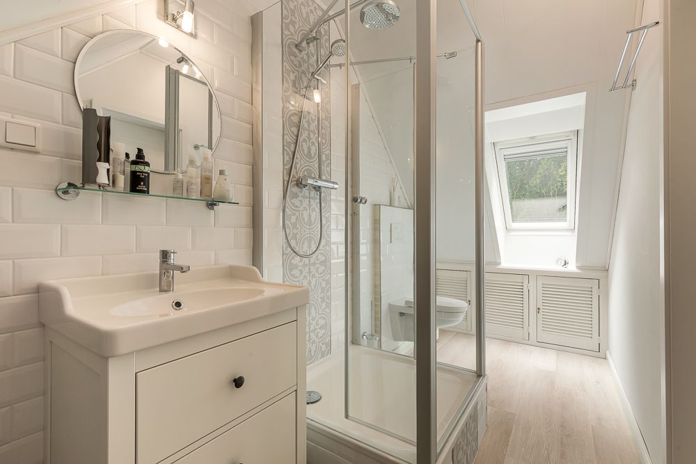 Modernes Badezimmer mit Dusche, Waschbecken, Spiegel und Fenster unter einer Dachschräge.