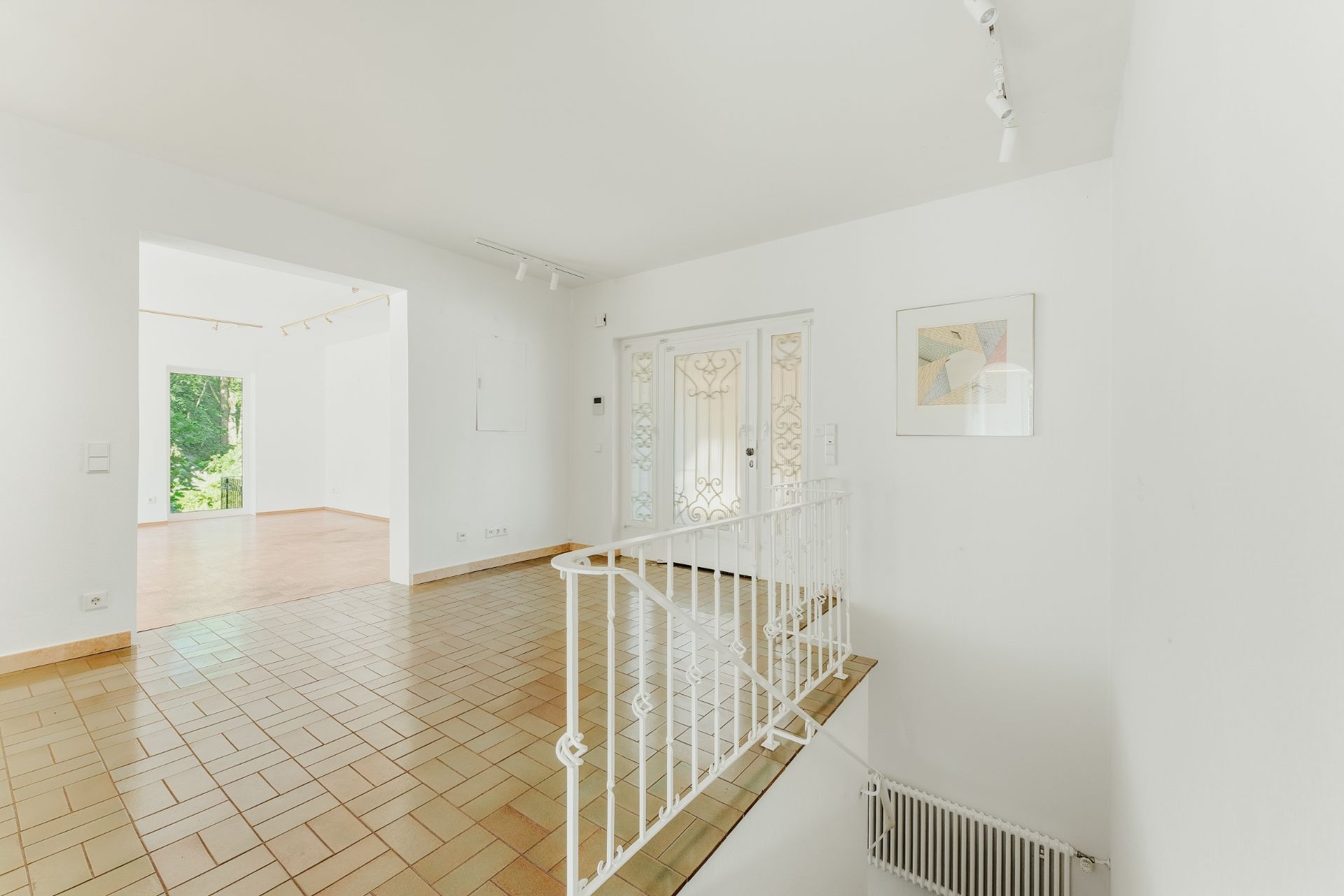 Heller Flur mit braunen Fliesen, weißem Geländer und Blick in ein weiteres Zimmer.