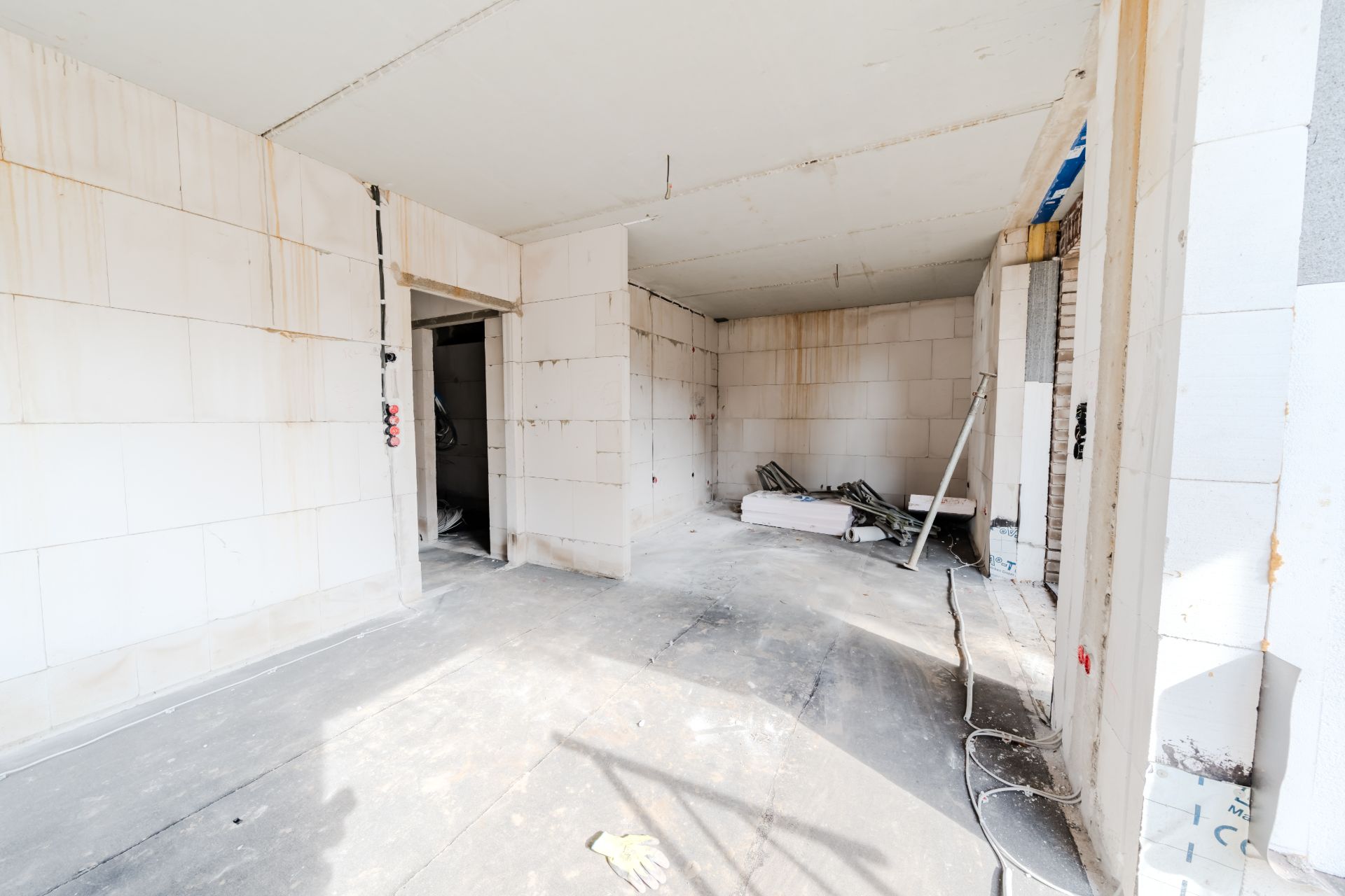 Leerer Raum mit weißen Wänden im Rohbau, Baumaterialien und Leiter an der Wand.