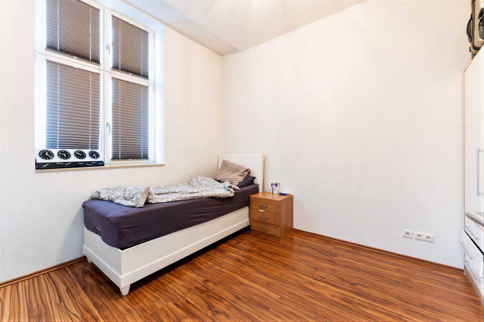 Schlafzimmer mit Einzelbett, Nachttisch und Fenster, Holzboden.