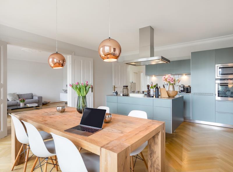 Cocina moderna con mesa de madera, sillas blancas y sala de estar al fondo.