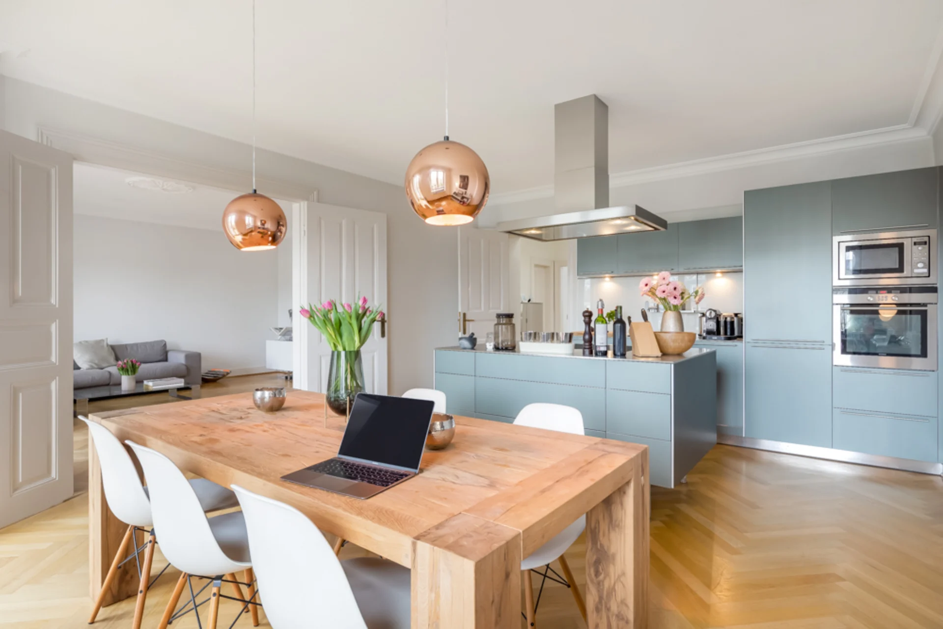 Moderne Küche mit Holztisch, weißen Stühlen und offenen Wohnbereich im Hintergrund.