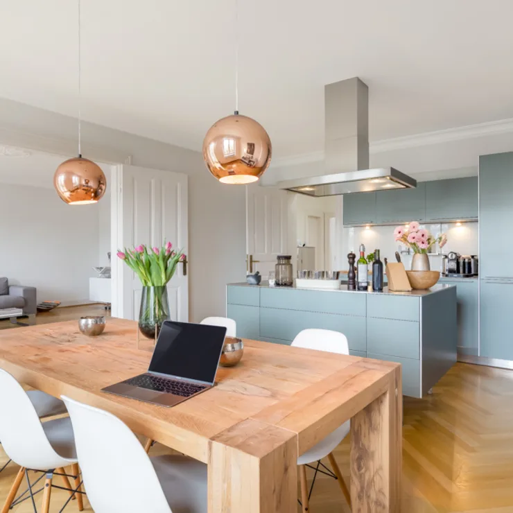 Moderne Küche mit Holztisch, weißen Stühlen und offenen Wohnbereich im Hintergrund.