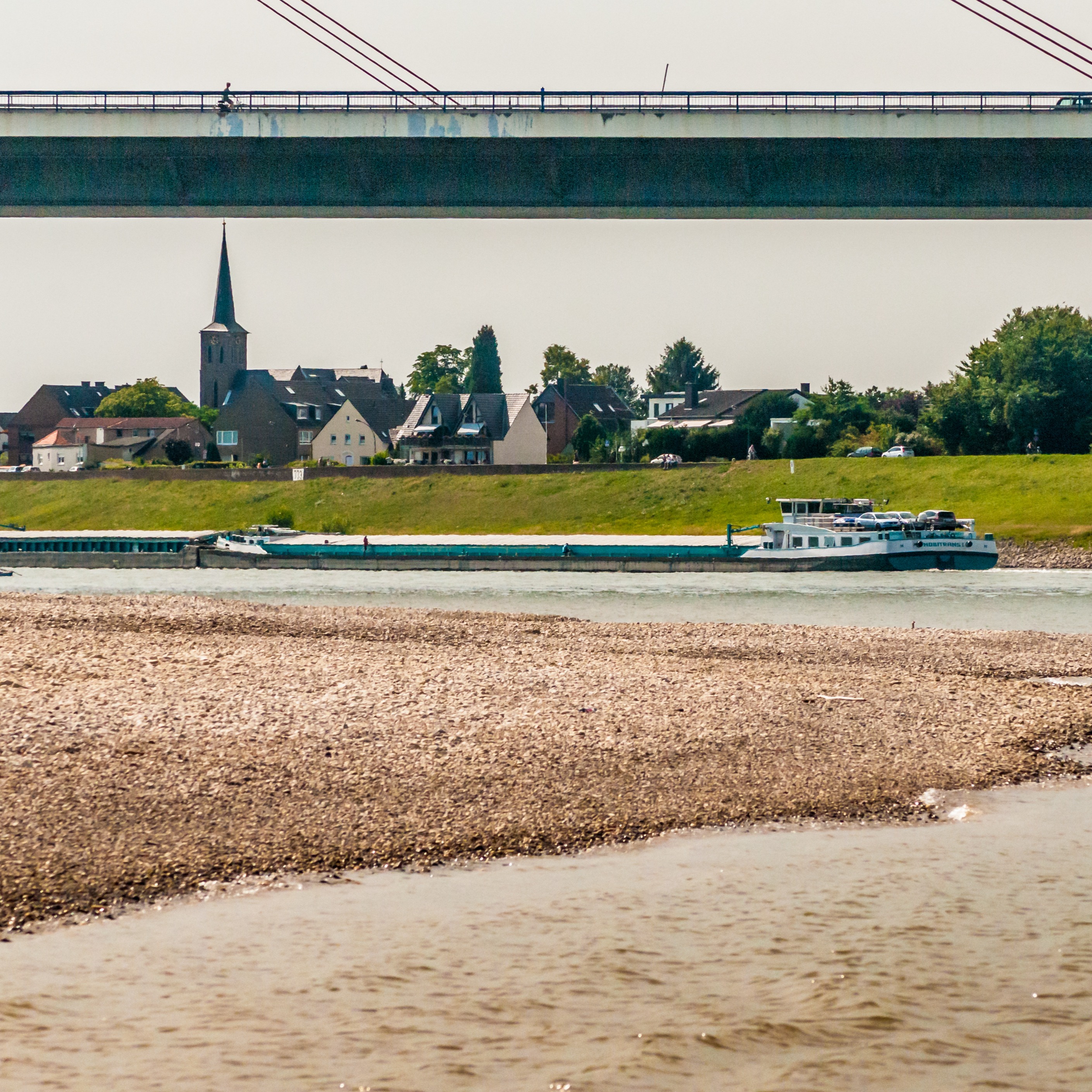 Brücke über einem Fluss, im Hintergrund Wohnhäuser und eine Kirche.