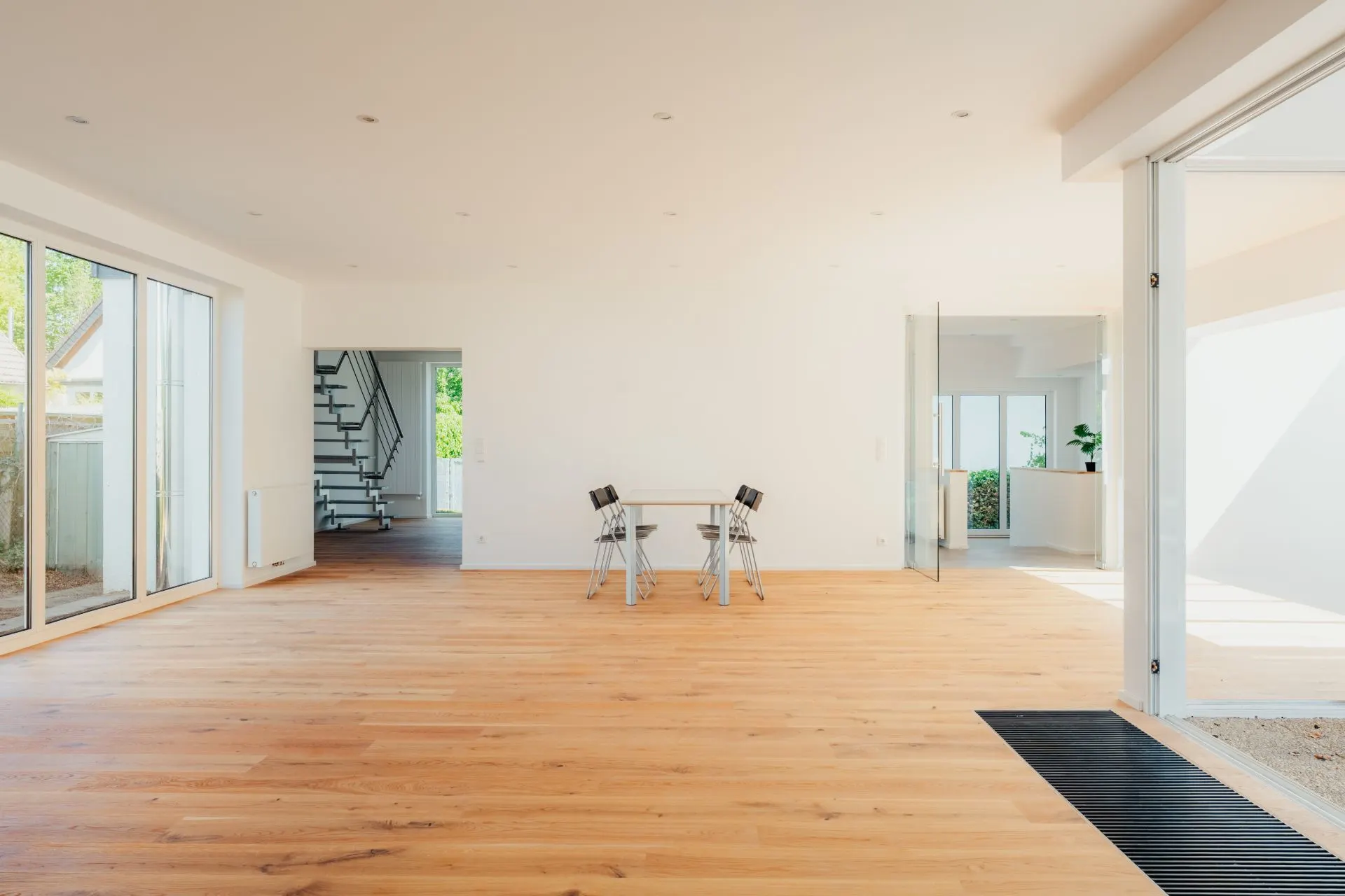 Helles Wohnzimmer mit Holzfußboden, Glastüren, kleinem Tisch und vier Stühlen.