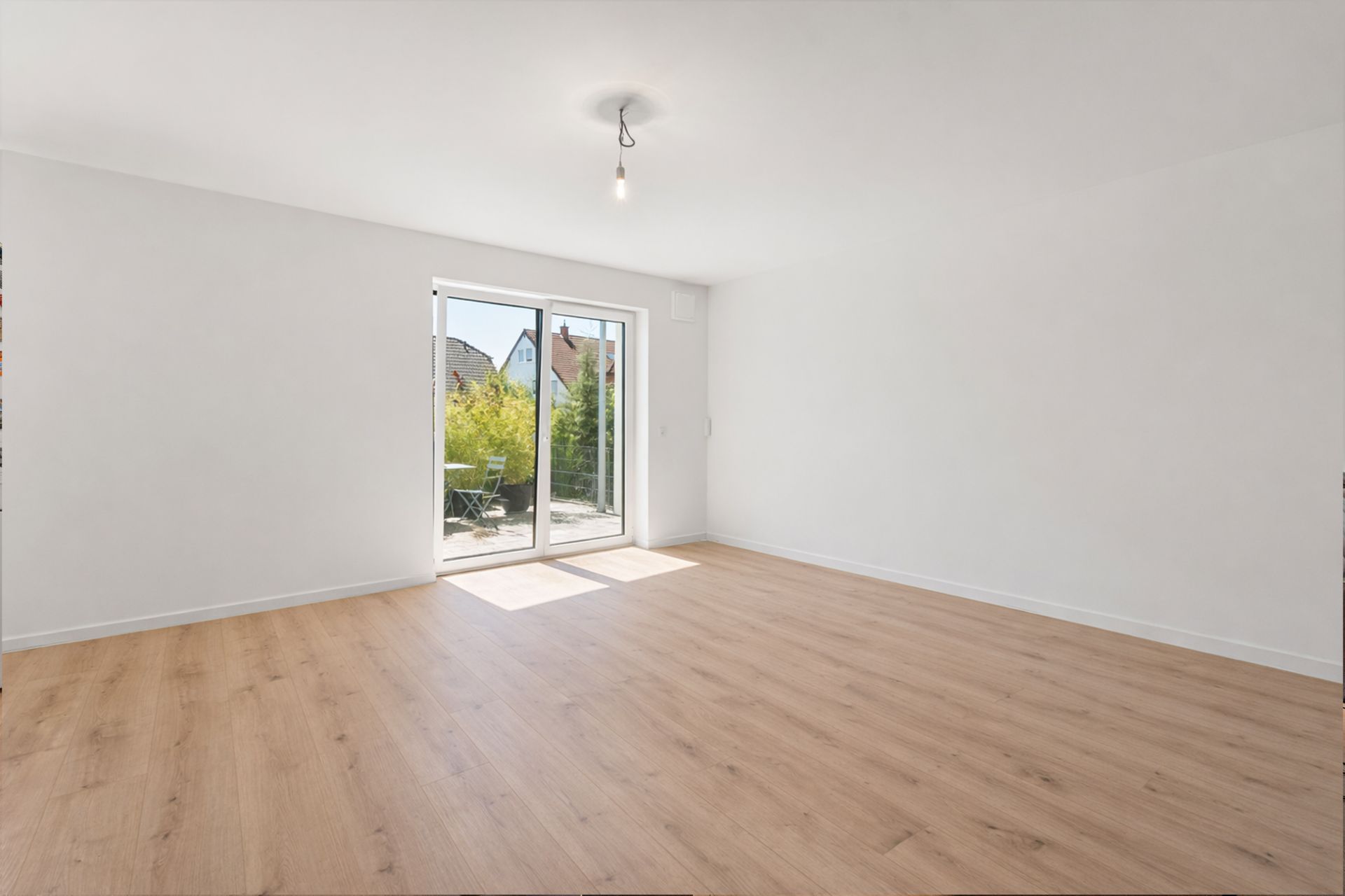 Helles, leeres Zimmer mit Holzfußboden und großen Glastüren zu einem Balkon.