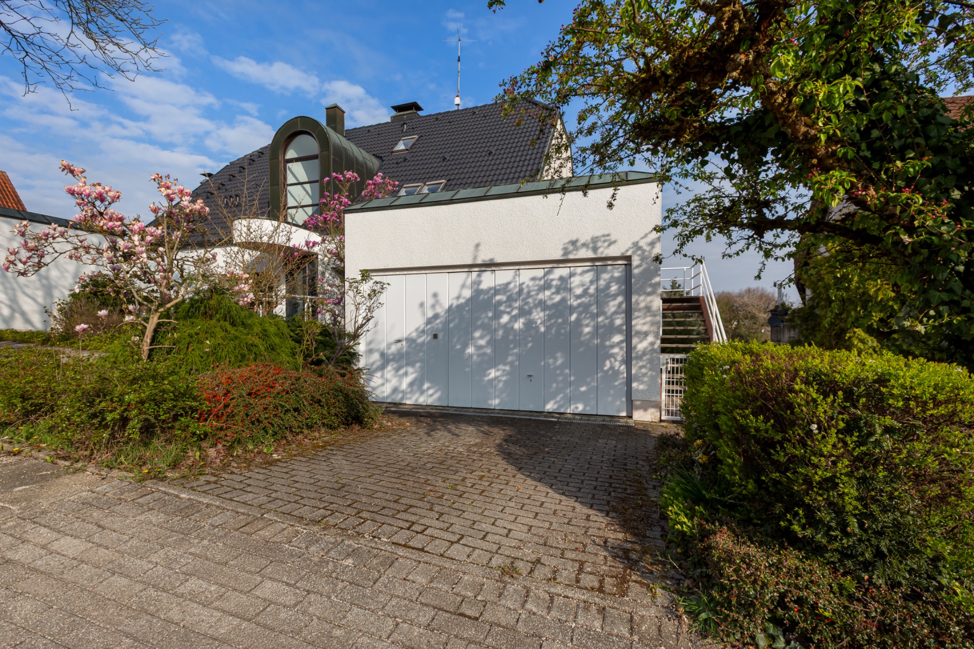 Einfamilienhaus mit Garage, bepflanztem Vorgarten und gepflasterter Einfahrt.