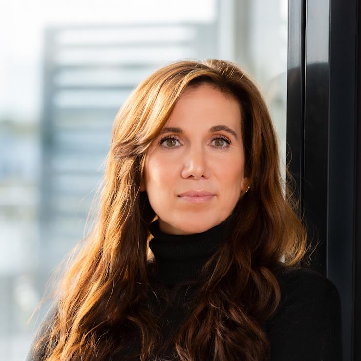 Frau mit langen braunen Haaren und schwarzem Pullover steht vor einem Fenster.