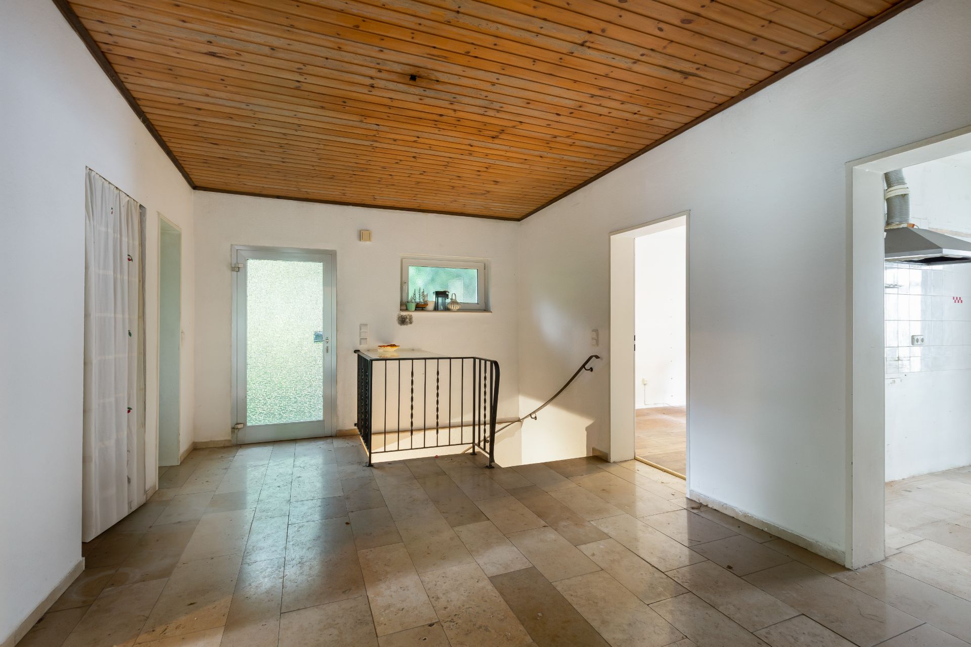 Heller Flur mit Holzbalkendecke, Steinfussboden und Treppe, Türen führen in andere Räume.