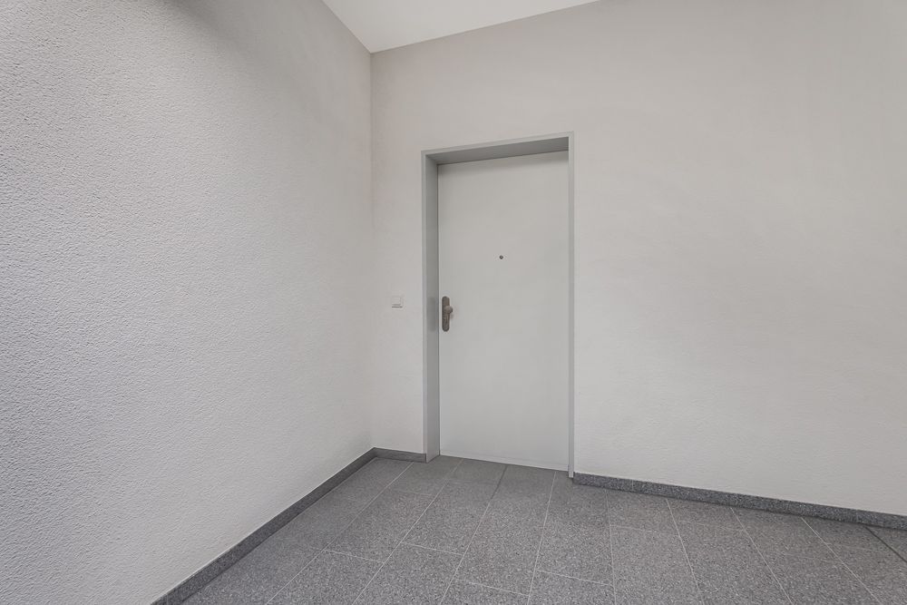 Heller Flur mit grauer Eingangstür und gefliestem Boden.