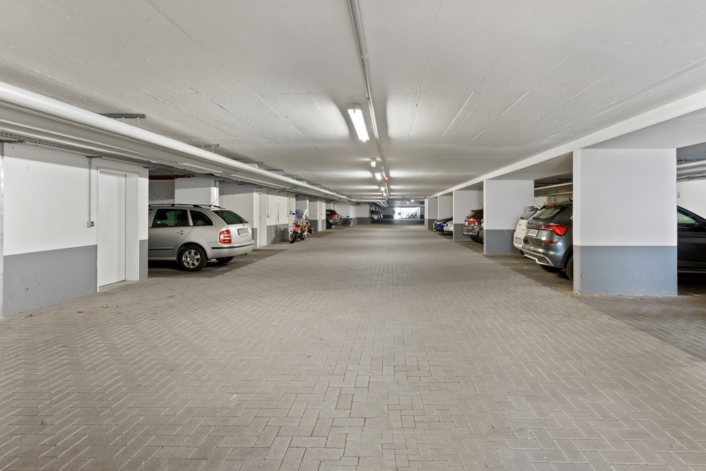 Helle Tiefgarage mit parkenden Autos und Motorrädern, weiße Wände und helle Beleuchtung.