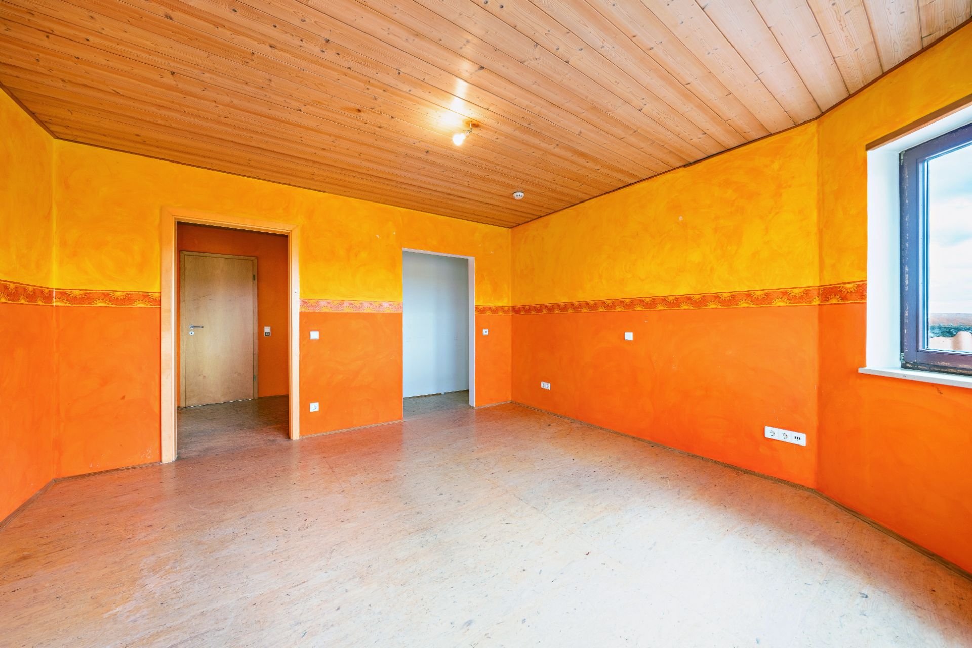 Leerer Raum mit gelb-orange gestrichenen Wänden, Holzdecke und Fenster.