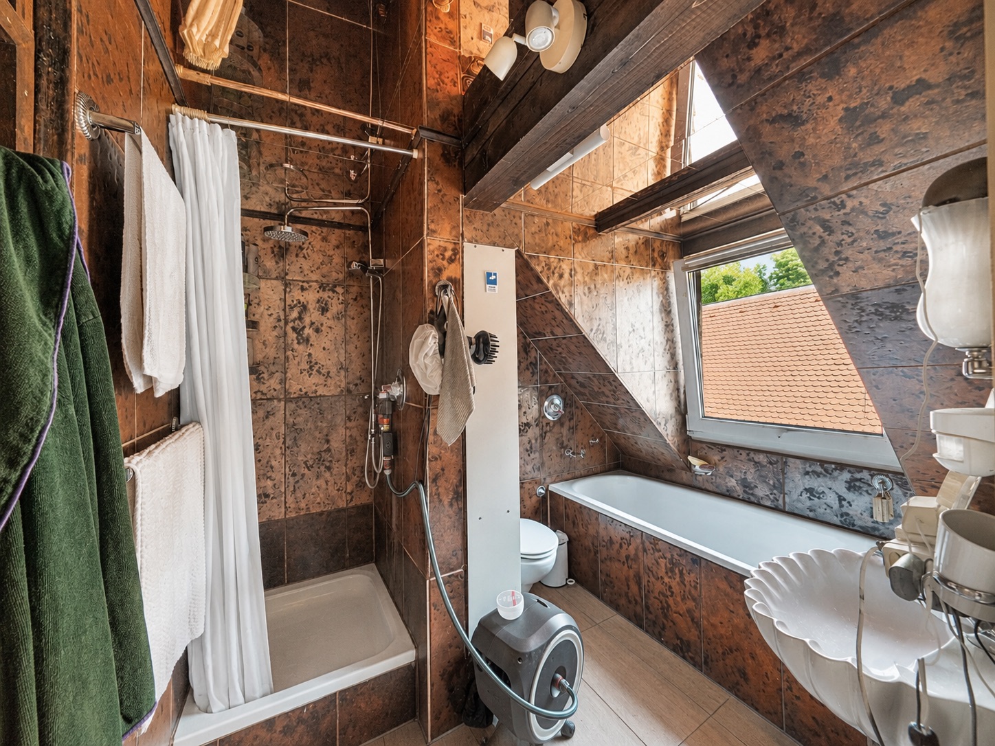 Badezimmer mit Dusche, Badewanne, Waschbecken und Fenster unter einer Dachschräge.
