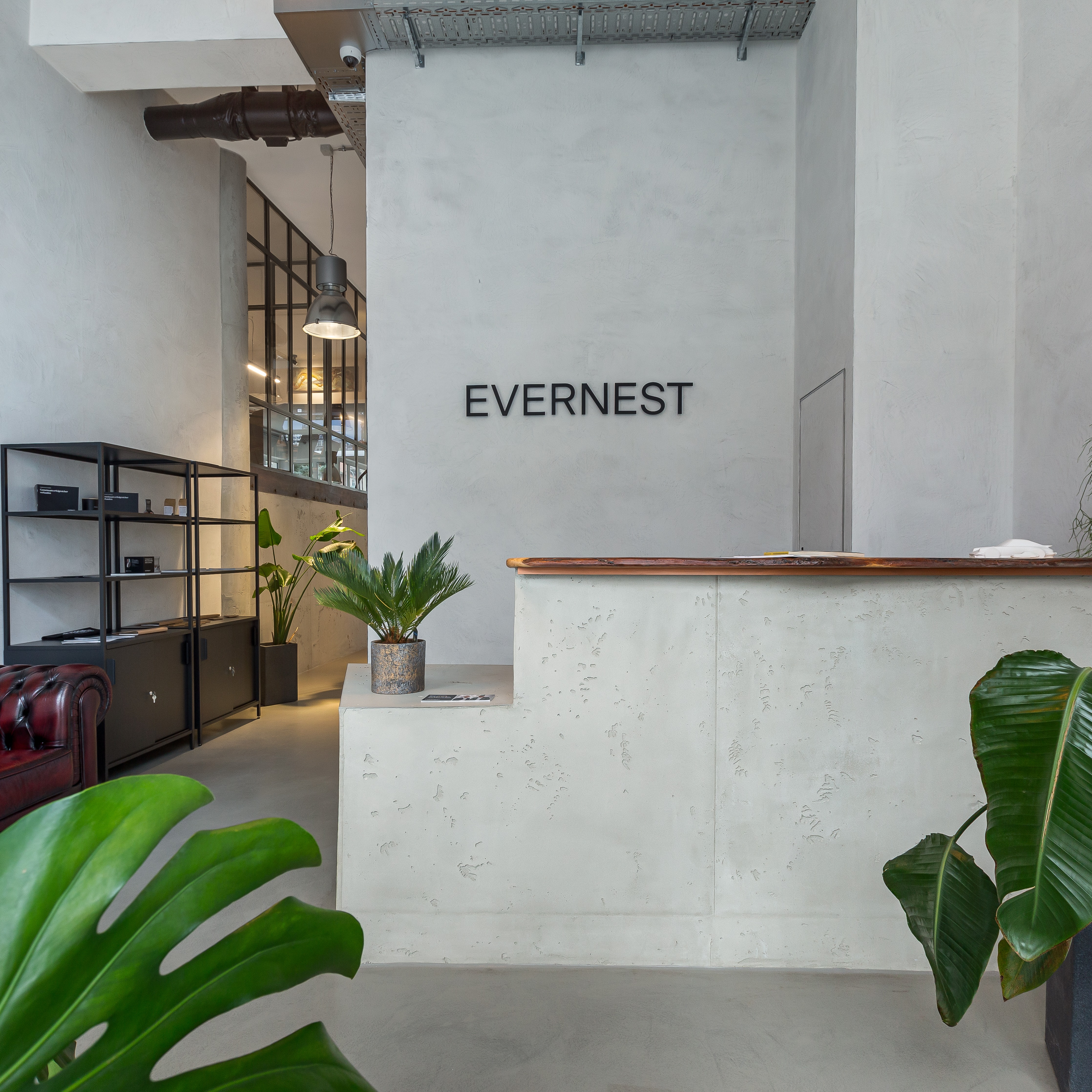 Moderner Eingangsbereich mit Pflanzen, Regal und Schreibtisch, Schriftzug 'EVERNEST' an der Wand.