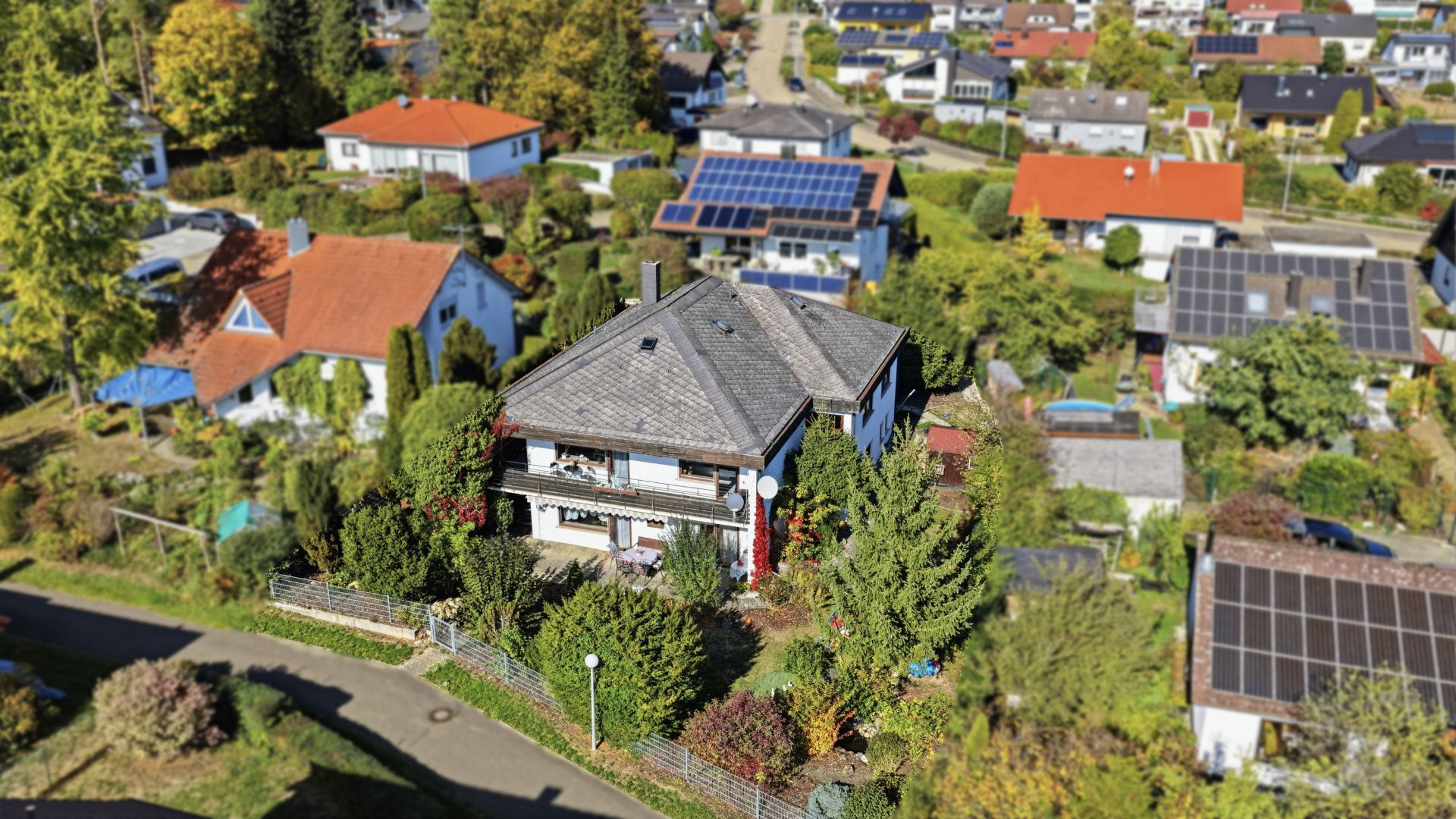 Luftaufnahme eines Wohnhauses mit Garten, umgeben von weiteren Häusern und viel Grün.