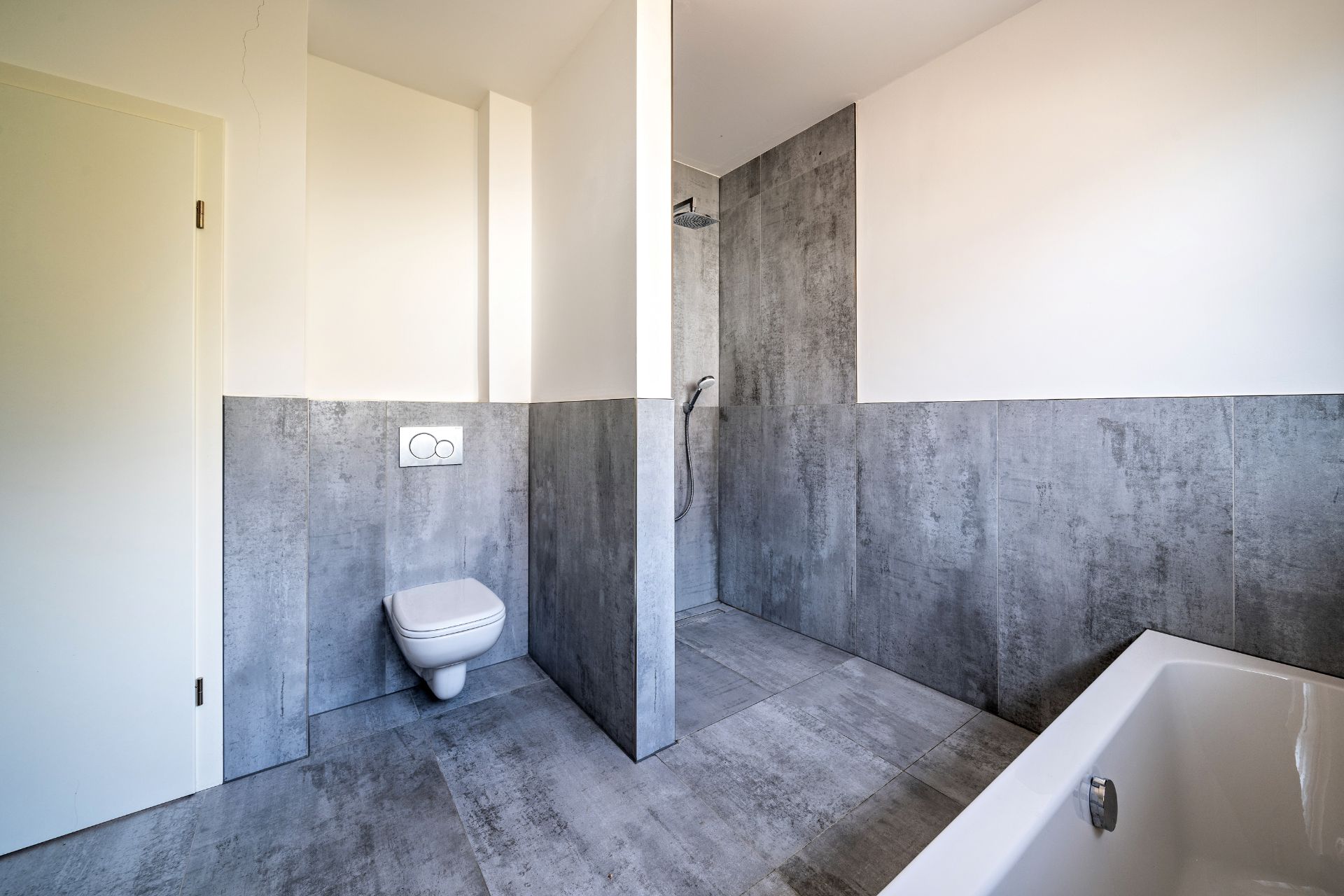 Modernes Badezimmer mit grauen Fliesen, Dusche, Wandtoilette und Badewanne.