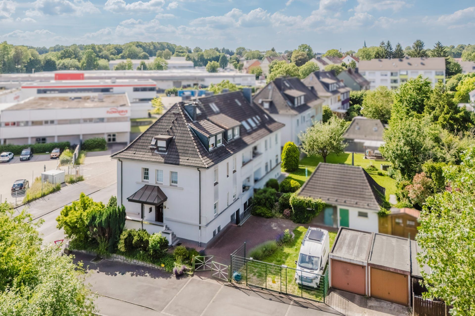 Mehrfamilienhaus mit Garten, Einfahrt und mehreren Garagen in einer Wohngegend bei sonnigem Wetter.