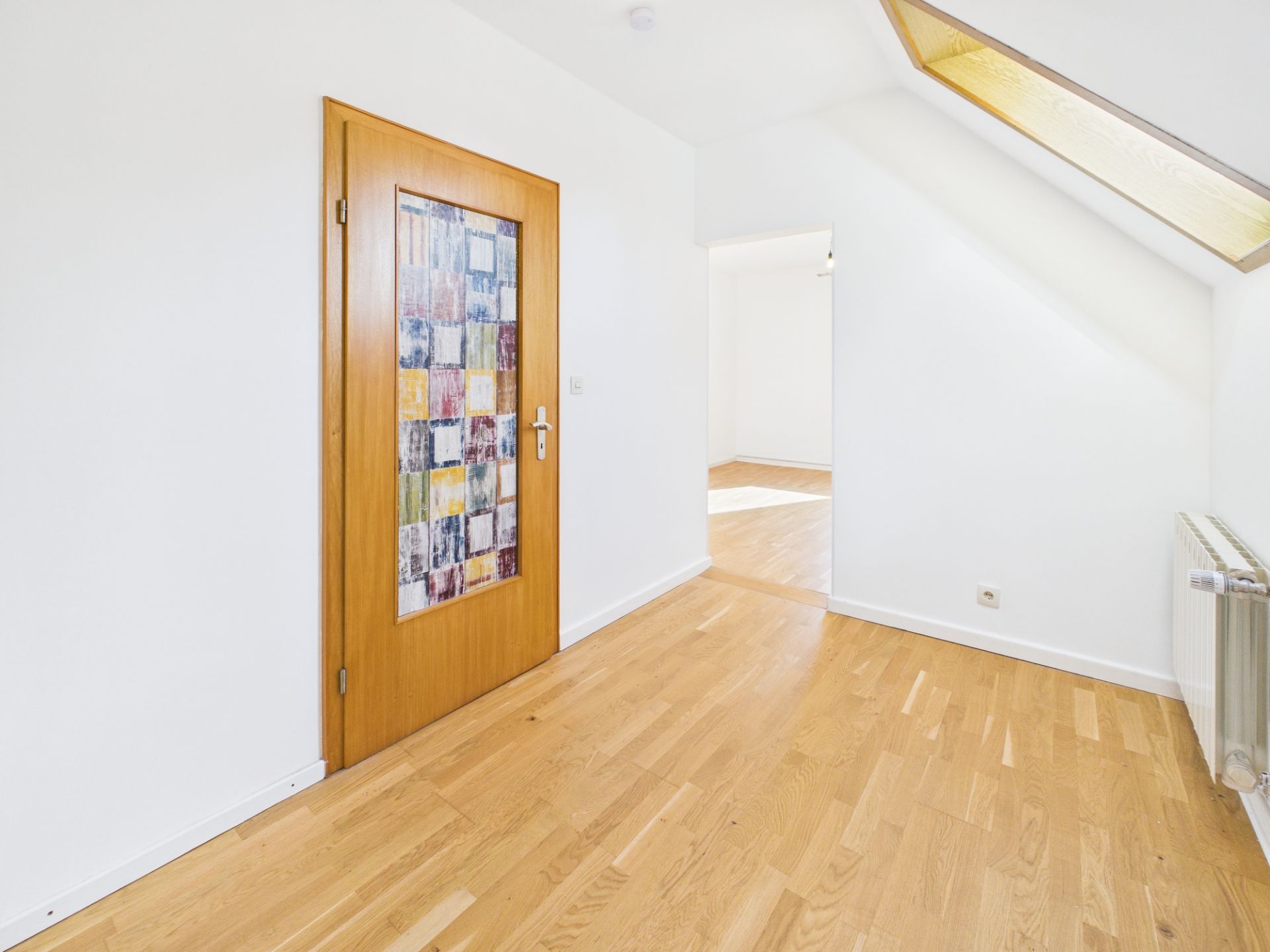 Heller Flur mit Parkettboden, Holztür mit buntem Glas und großem Dachfenster.