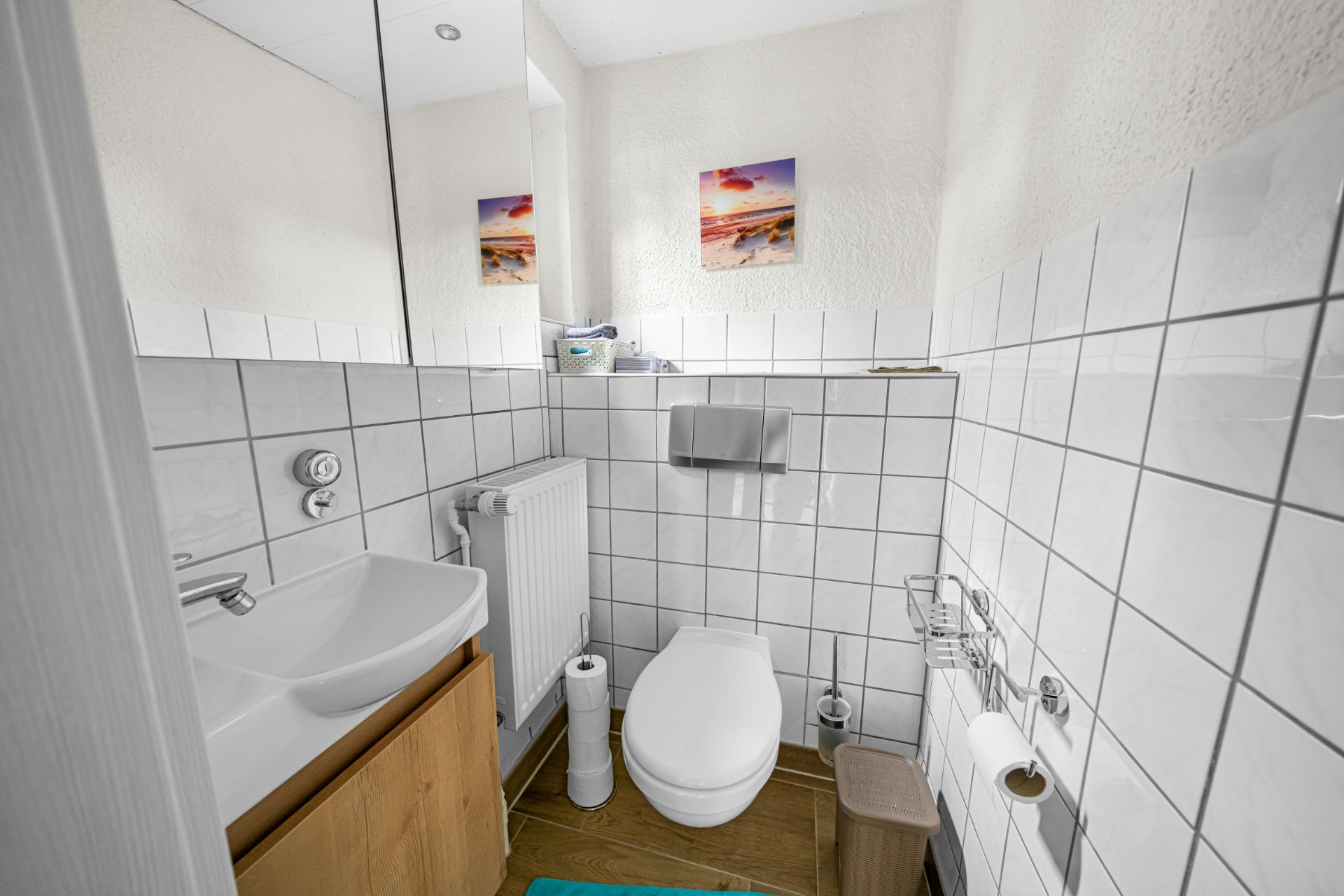 Kleines Badezimmer mit Waschbecken, Toilette, Heizkörper und weiß gefliesten Wänden.