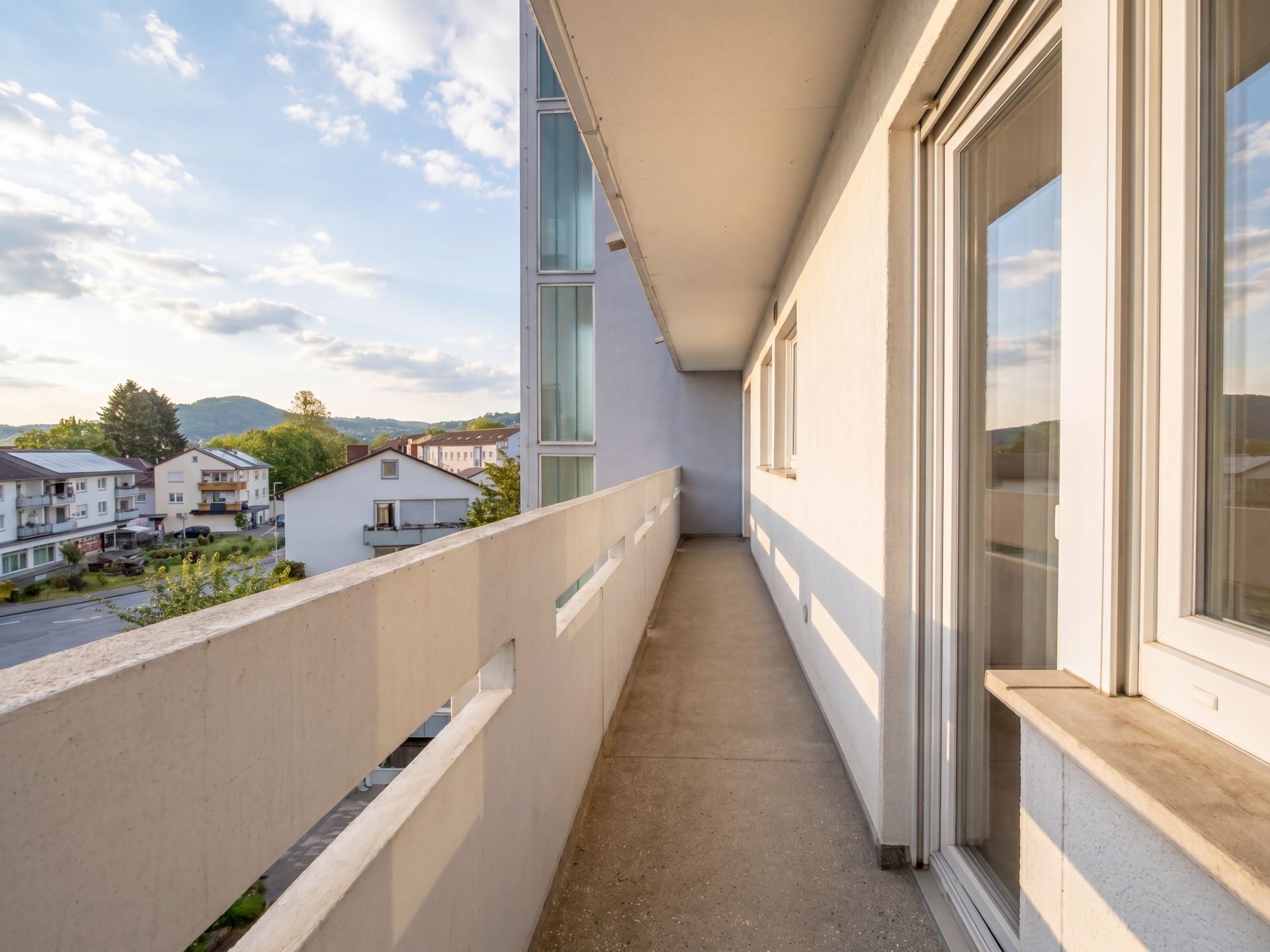 Langer, überdachter Balkon mit Blick auf Wohnhäuser und Berge im Hintergrund.