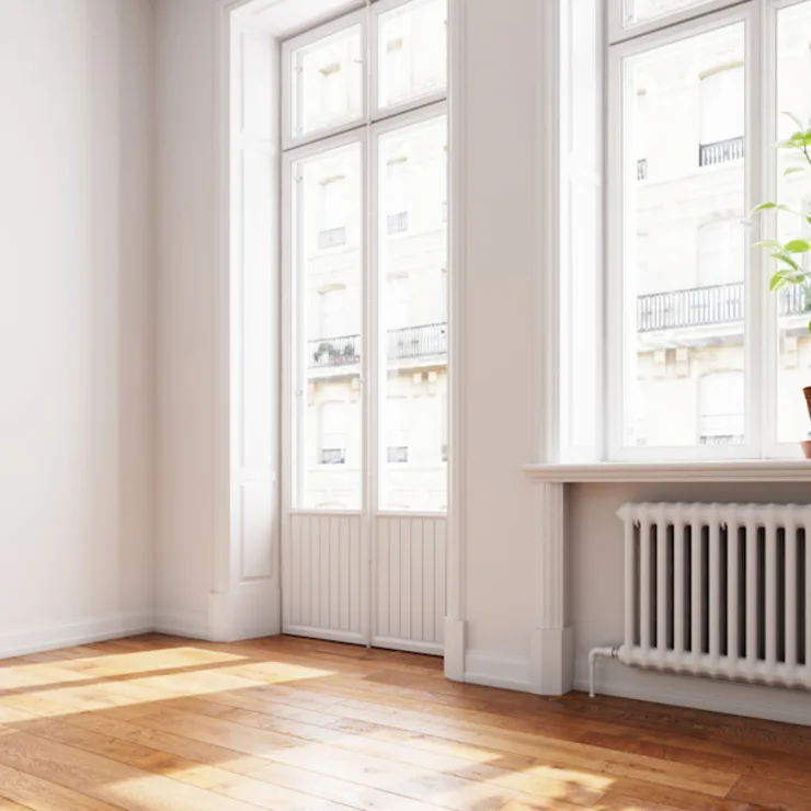 Heller Raum mit großen Fenstern, Parkettboden und einer Pflanze auf der Fensterbank.