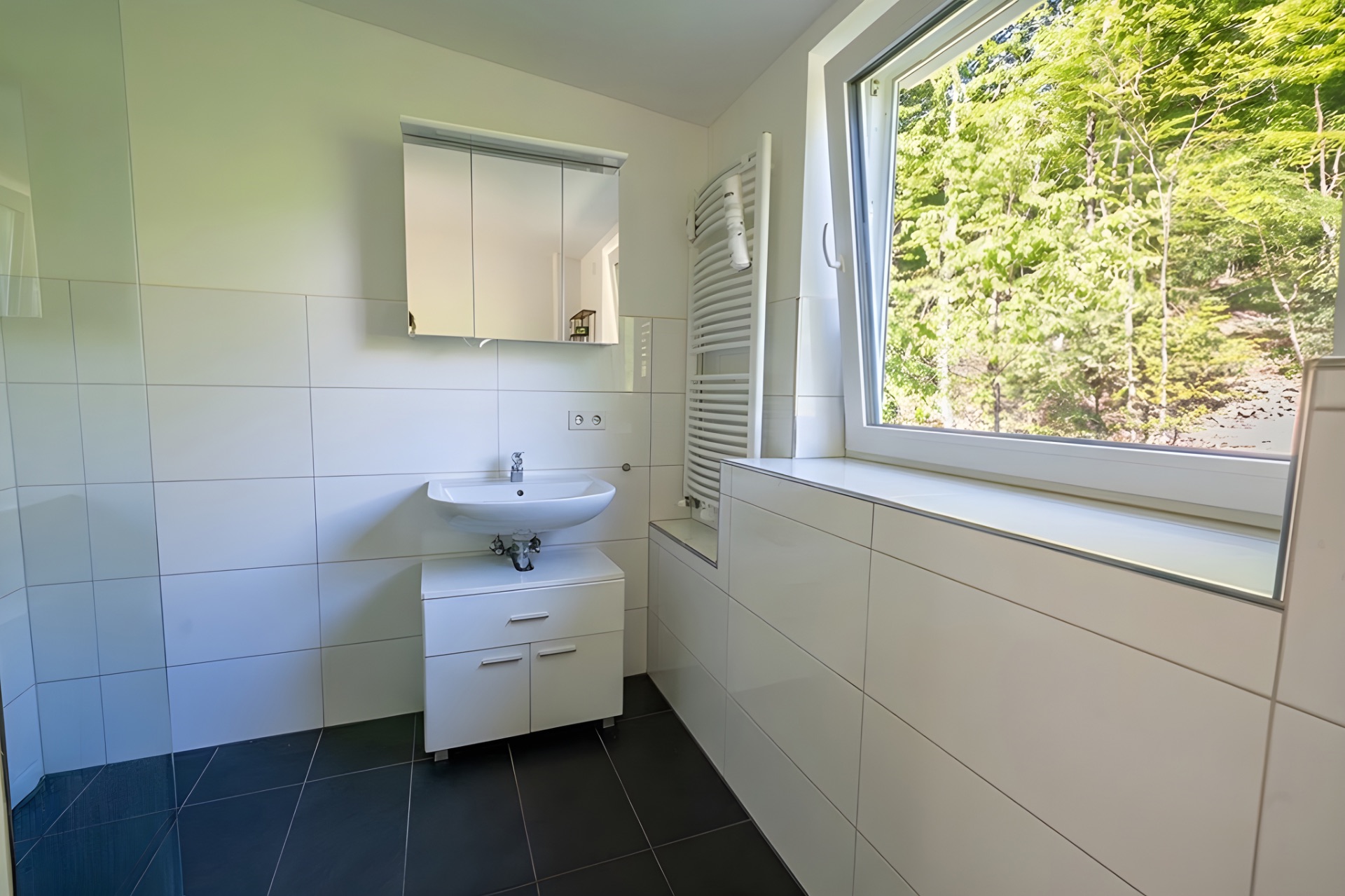 Modernes Badezimmer mit Waschbecken, Spiegelschrank und großem Fenster mit Blick ins Grüne.