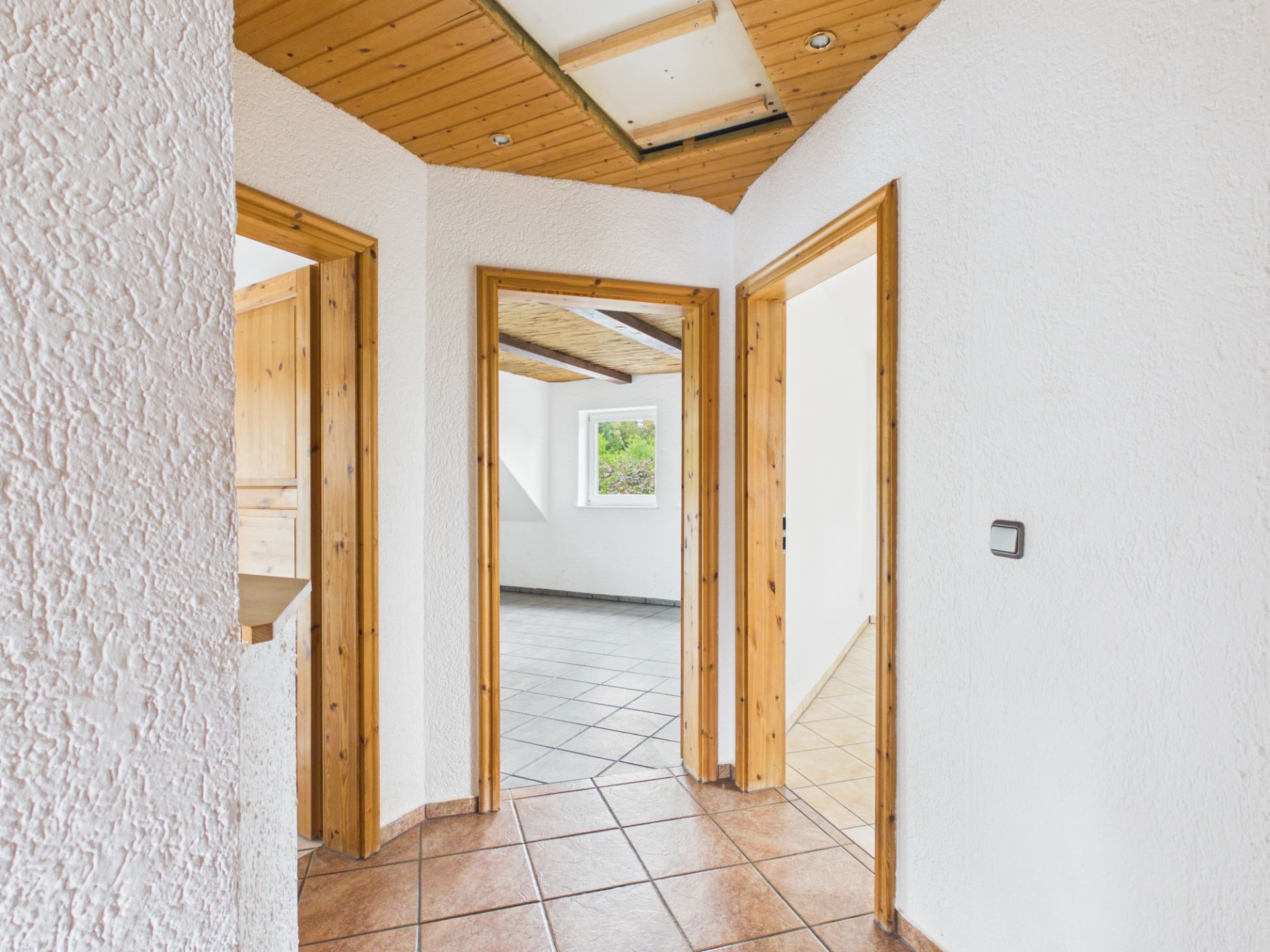 Flur mit drei offenen Türen und Fliesenboden, dahinter helle Zimmer mit Fenstern.