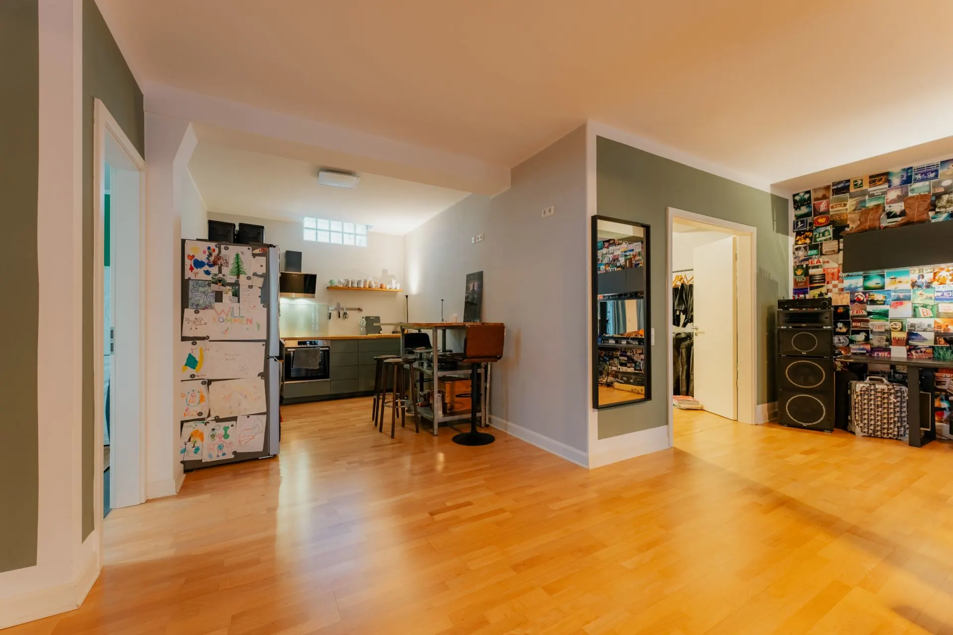 Wohnzimmer mit Holzboden, offener Küche, buntem Kühlschrank und Wand mit Fotos.