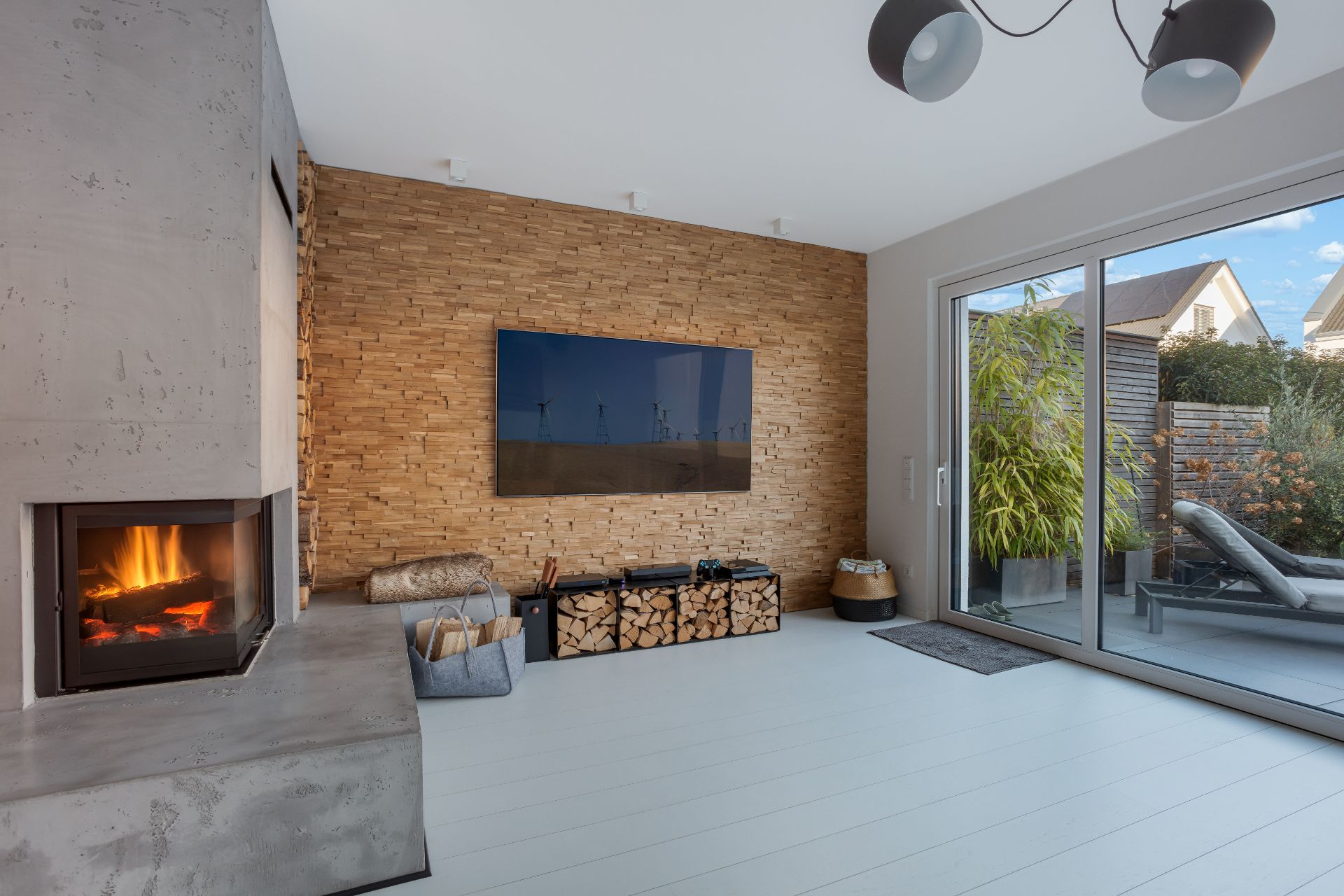 Modernes Wohnzimmer mit Kamin, Holzwand, Fernseher und Zugang zur Terrasse.