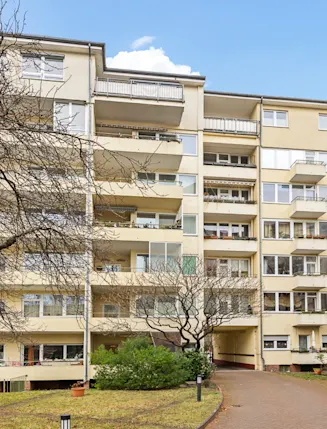 Mehrstöckiges Wohngebäude mit Balkonen, Bäumen und Fahrradständern im Vordergrund.