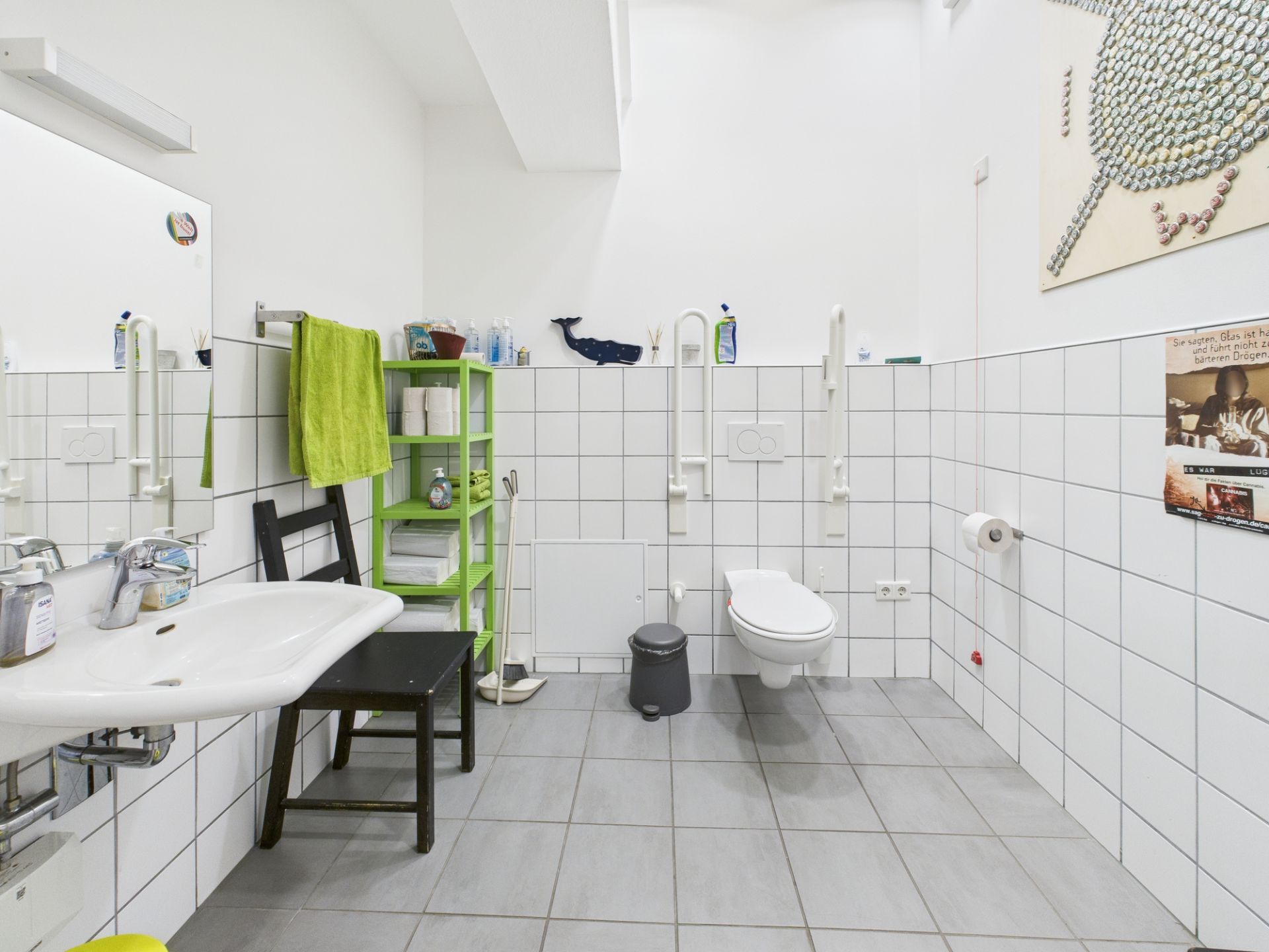 Barrierefreies Badezimmer mit Haltegriffen, Waschbecken, Regal und Wandbildern.
