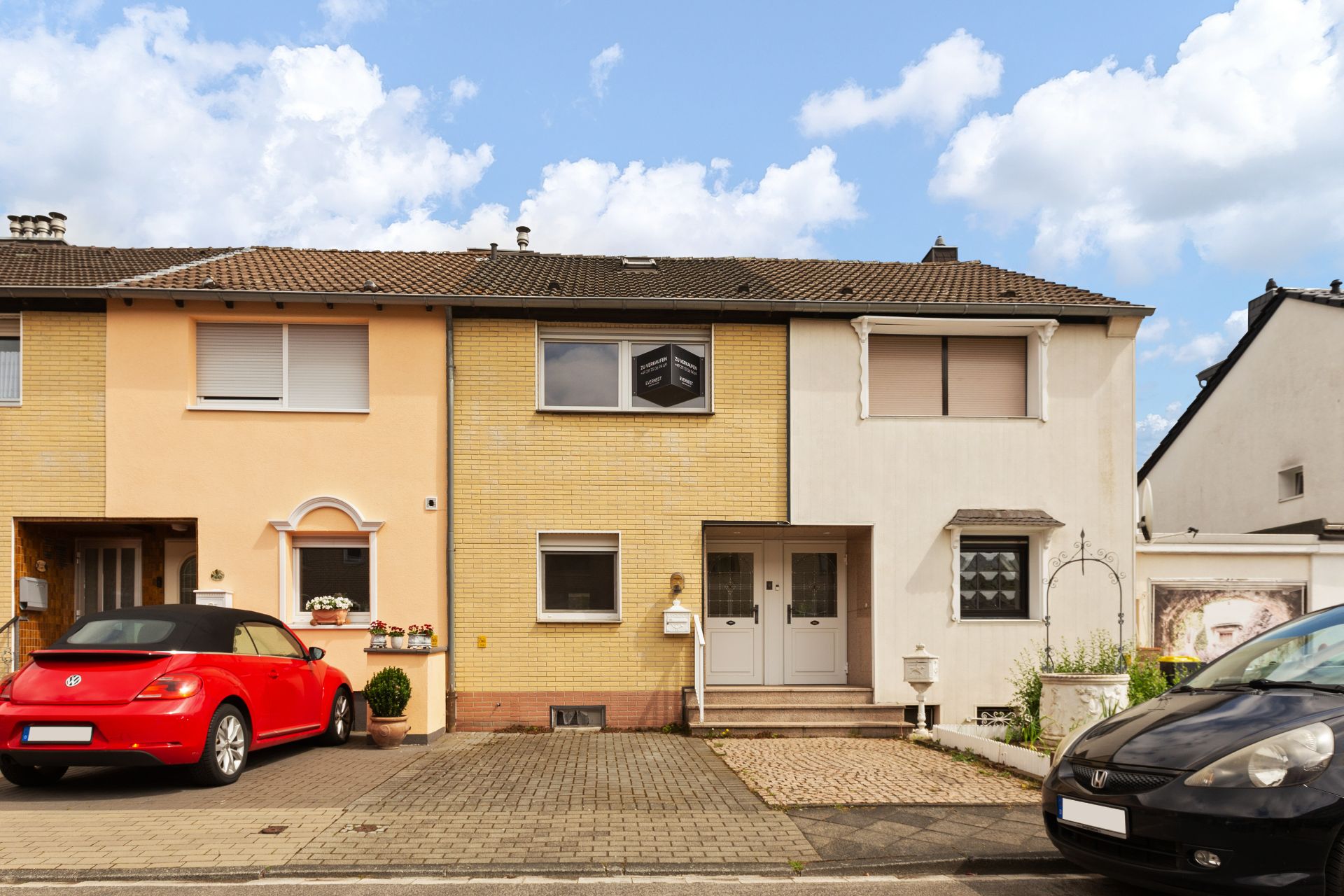 Reihenhaus mit gelber Fassade, zwei Eingängen und zwei geparkten Autos davor.