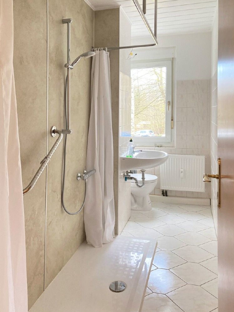 Helles Badezimmer mit Dusche, Duschvorhang, Waschbecken und Fenster.