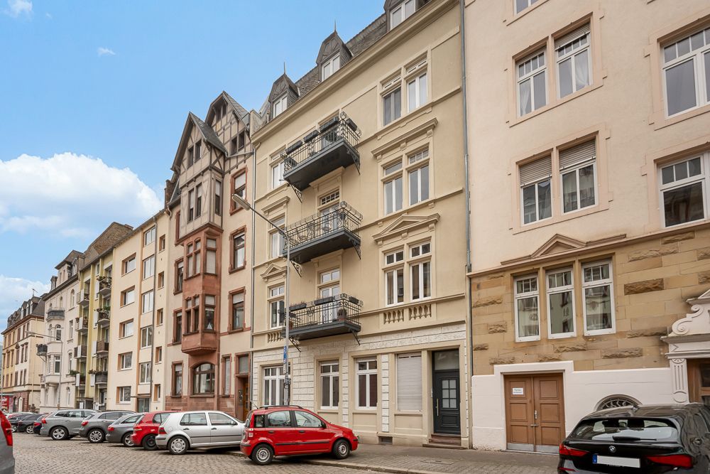 Mehrstöckige Wohnhäuser mit Balkonen in einer ruhigen Straße, mehrere geparkte Autos vorne.