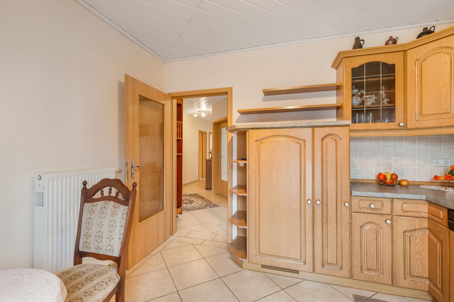Küche mit Holzschränken, Esstisch und Blick in den Flur eines Wohnhauses.
