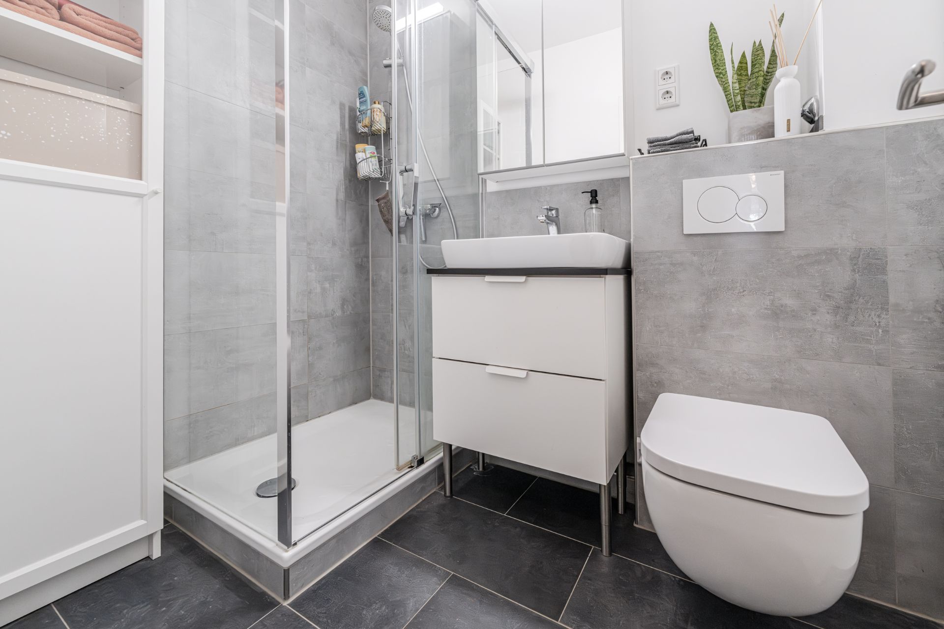 Modernes Bad mit Dusche, Waschbecken, Hängetoilette und Regal mit Handtüchern.