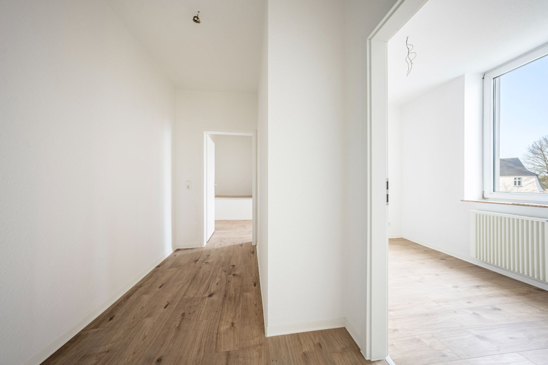 Heller Flur mit Holzboden, zwei offenen Türen und großem Fenster.