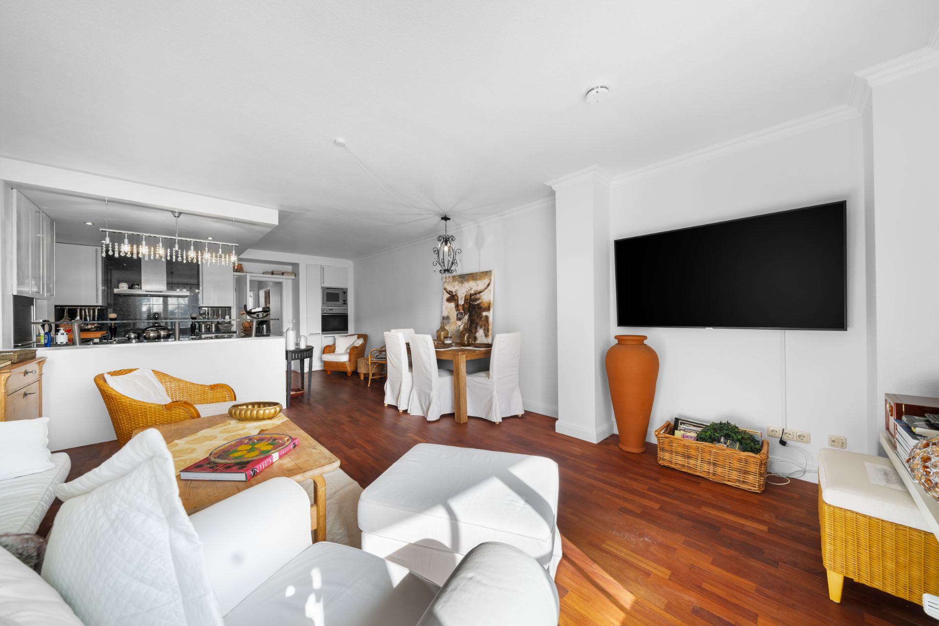 Helles Wohnzimmer mit offener Küche, Esstisch, großem Fernseher und Holzboden.