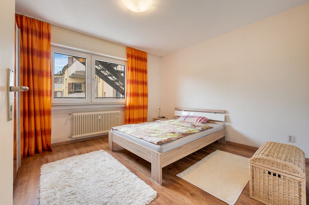 Schlafzimmer mit Holzboden, Doppelbett, orangenen Vorhängen und zwei Teppichen.