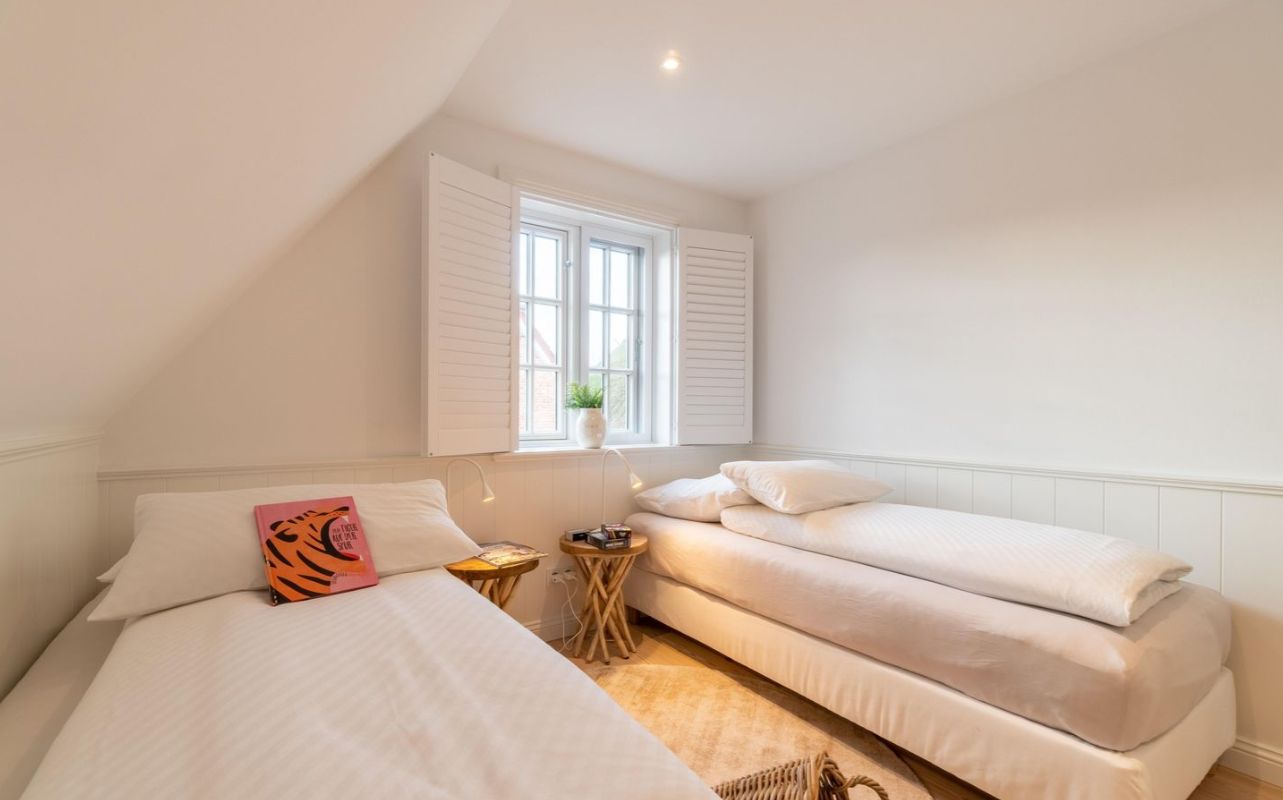 Helles Schlafzimmer mit zwei Einzelbetten, Fenster mit weißen Läden und kleinem Tisch dazwischen.