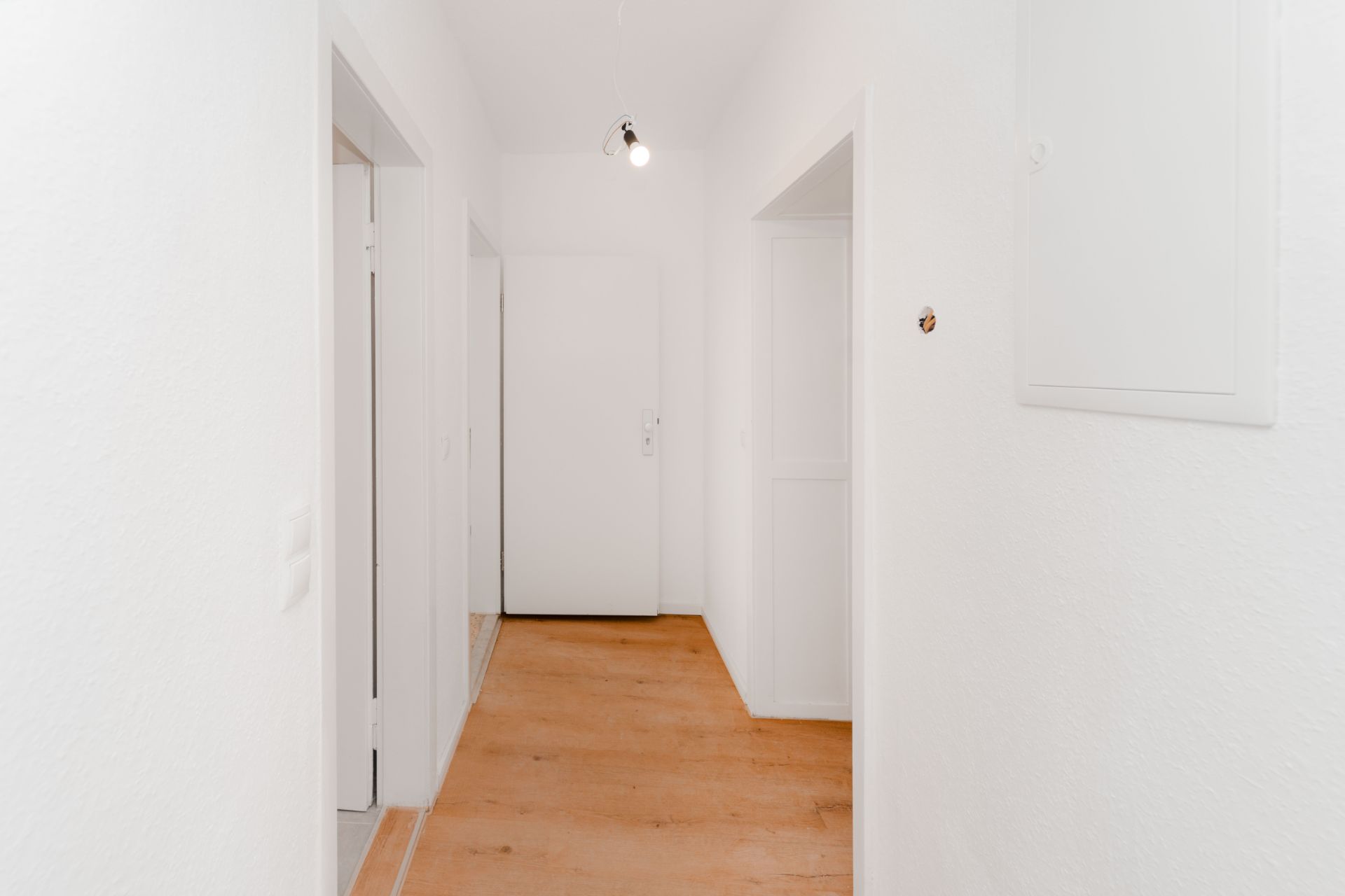 Heller Flur mit Holzboden, weißen Wänden und mehreren Türen.