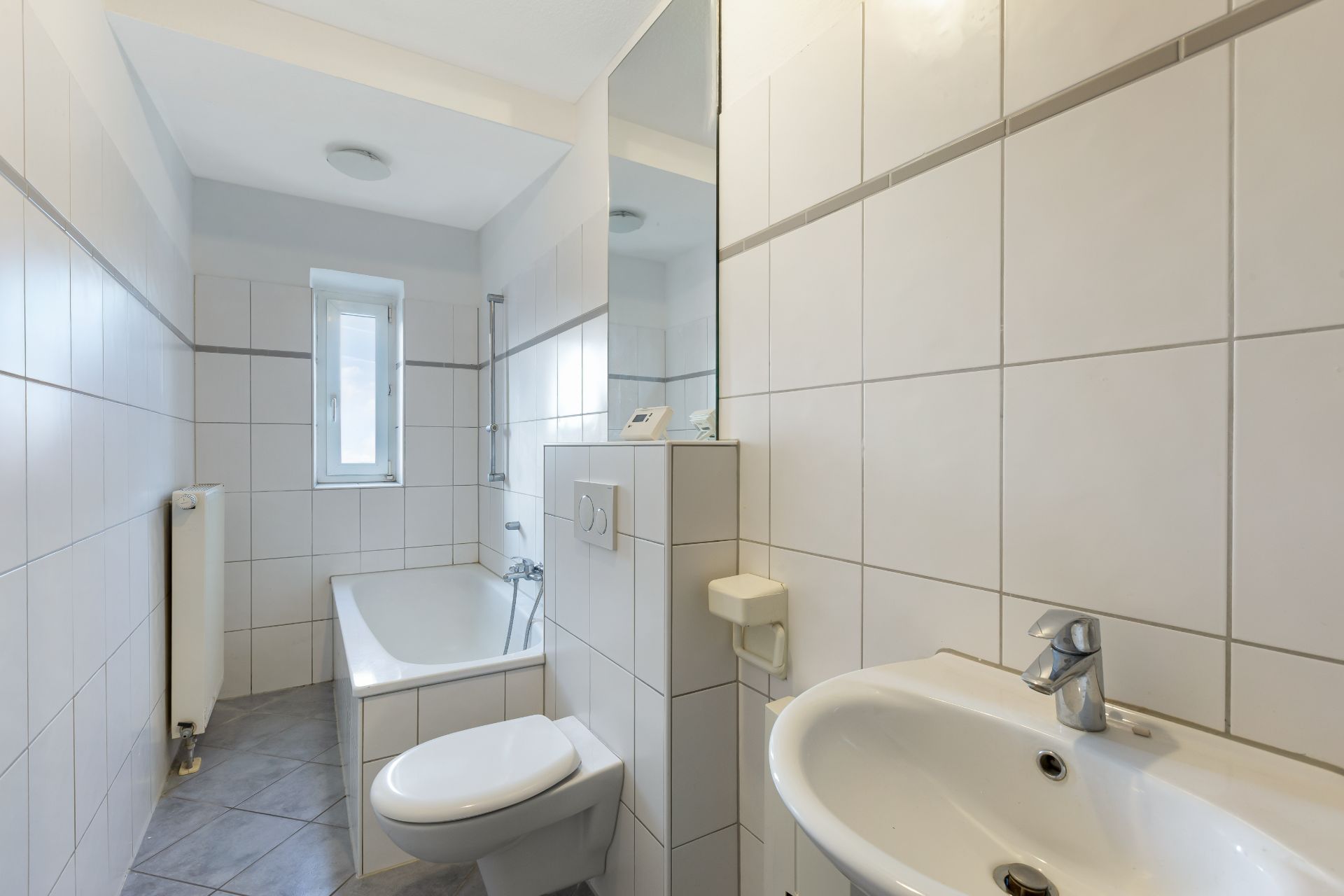 Helles Bad mit Badewanne, Waschbecken, Toilette und kleinem Fenster.