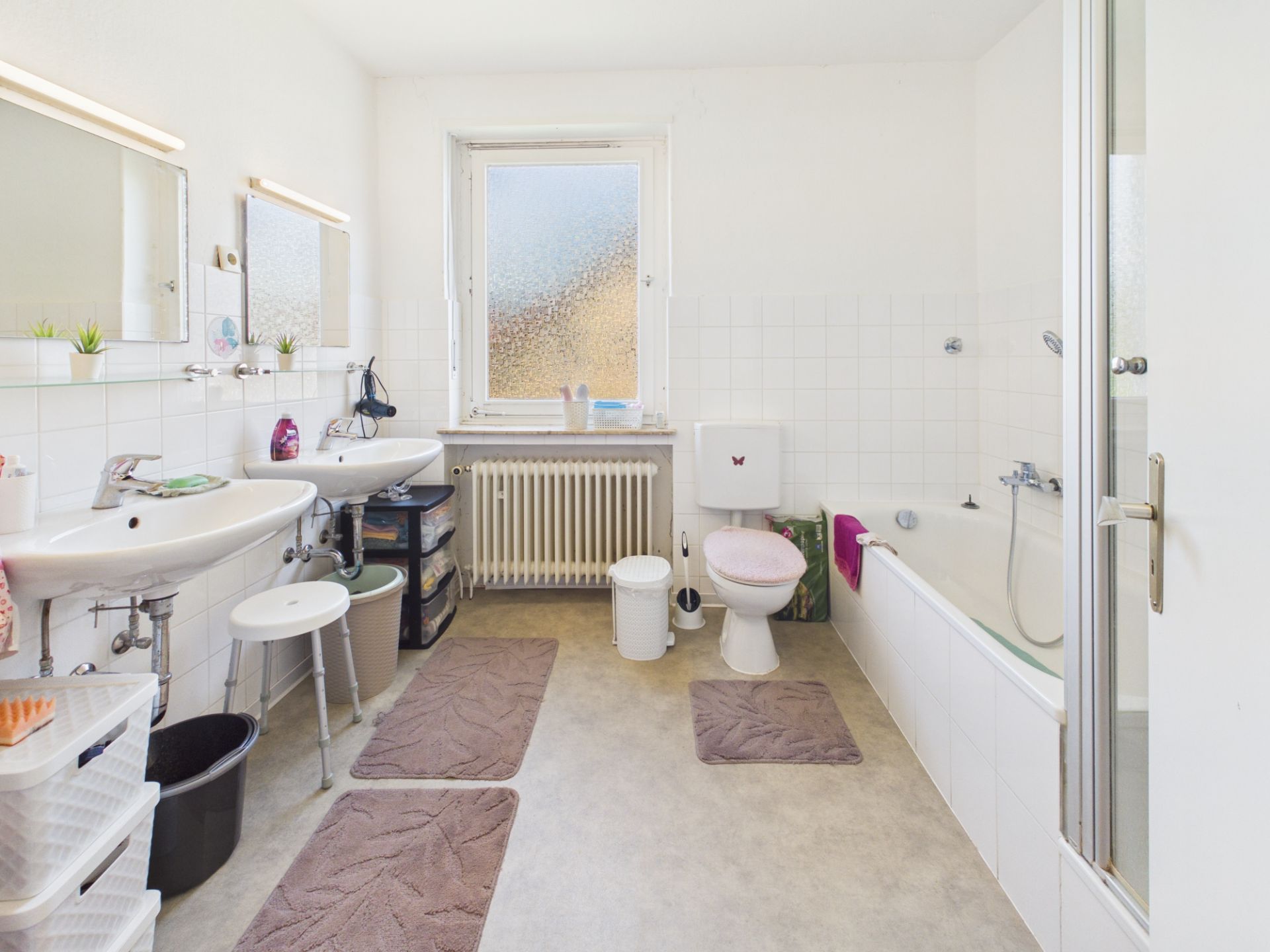 Helles Badezimmer mit zwei Waschbecken, Badewanne, WC, Fenster und Ablagen.